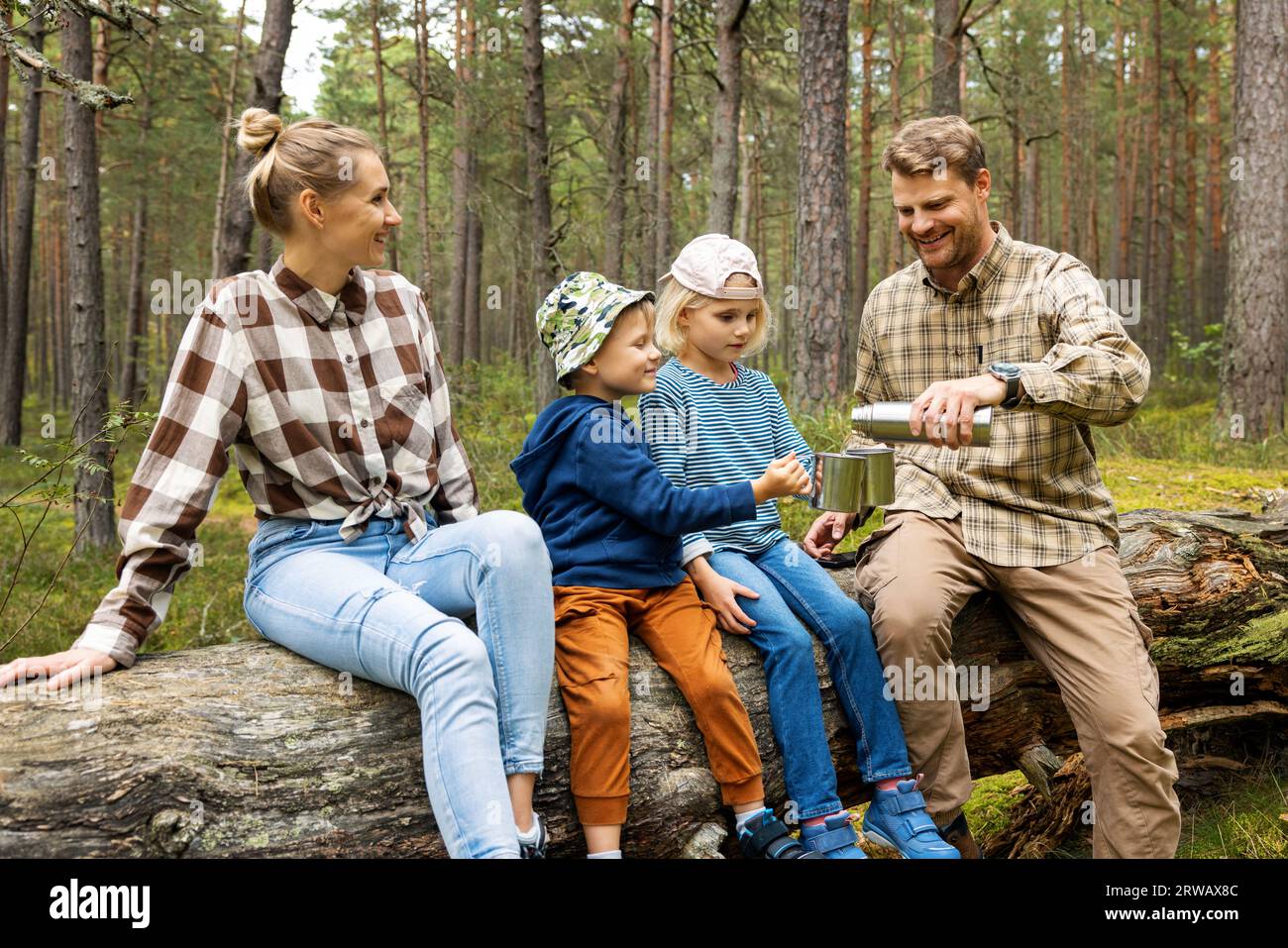 Familie mit Kindern, die nach einem Waldspaziergang auf umgestürzten Bäumen ein kleines Picknick machen. Tee aus Thermoskannen trinken. Aktivitäten im Freien Stockfoto