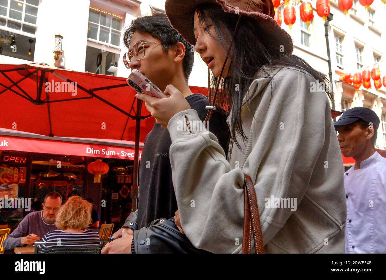 London, Großbritannien. Ein junges chinesisches Paar in Chinatown. Frau, die ihr Telefon überprüft Stockfoto