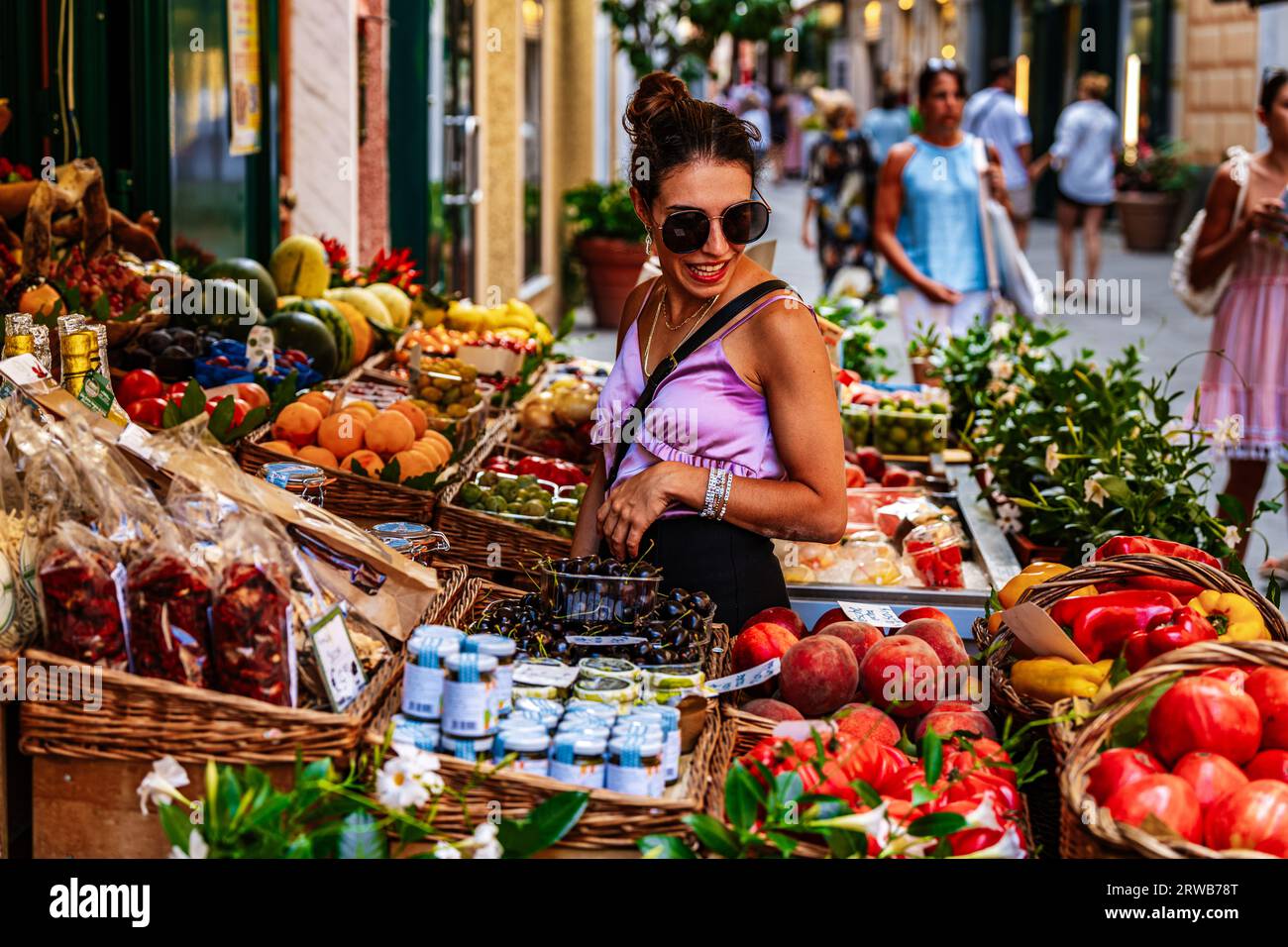 Eine gut gekleidete, schöne junge, elegante Frau, die frisches Obst und Gemüse an einem Obststand auf dem offenen Markt kauft. Stockfoto
