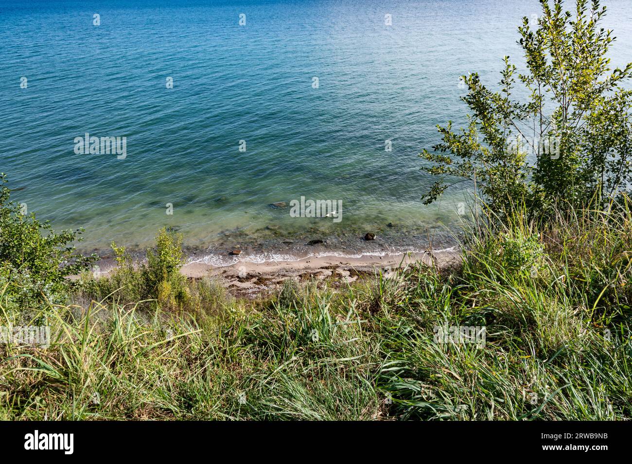 Gräser oben in der Tiefe ein Natur belassener Sandstrand. Die Ostsee schimmert in verschiedenen Farben Stockfoto