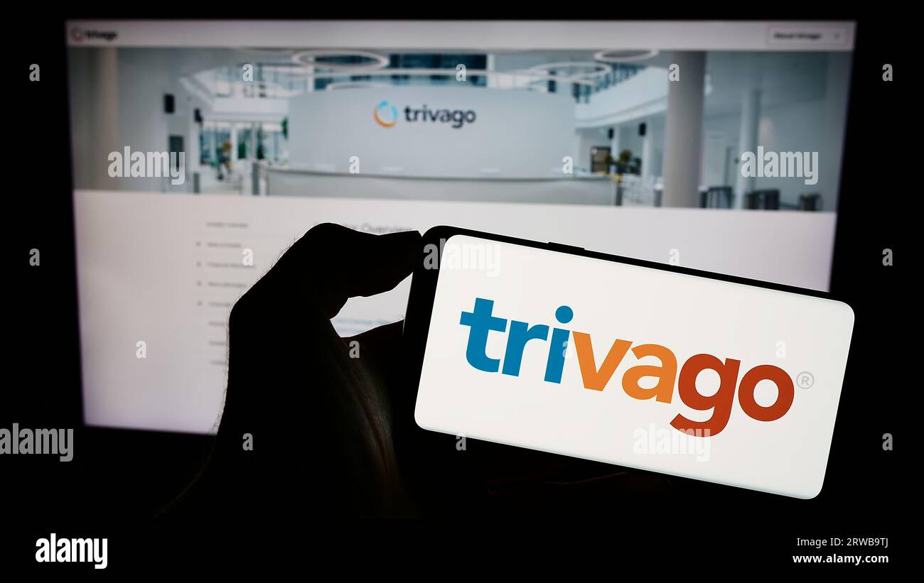 Person, die ein Mobiltelefon mit dem Logo der deutschen Hotelmetasuchfirma Trivago NV auf dem Bildschirm vor der Geschäftswebseite hält. Konzentrieren Sie sich auf das Display des Telefons. Stockfoto