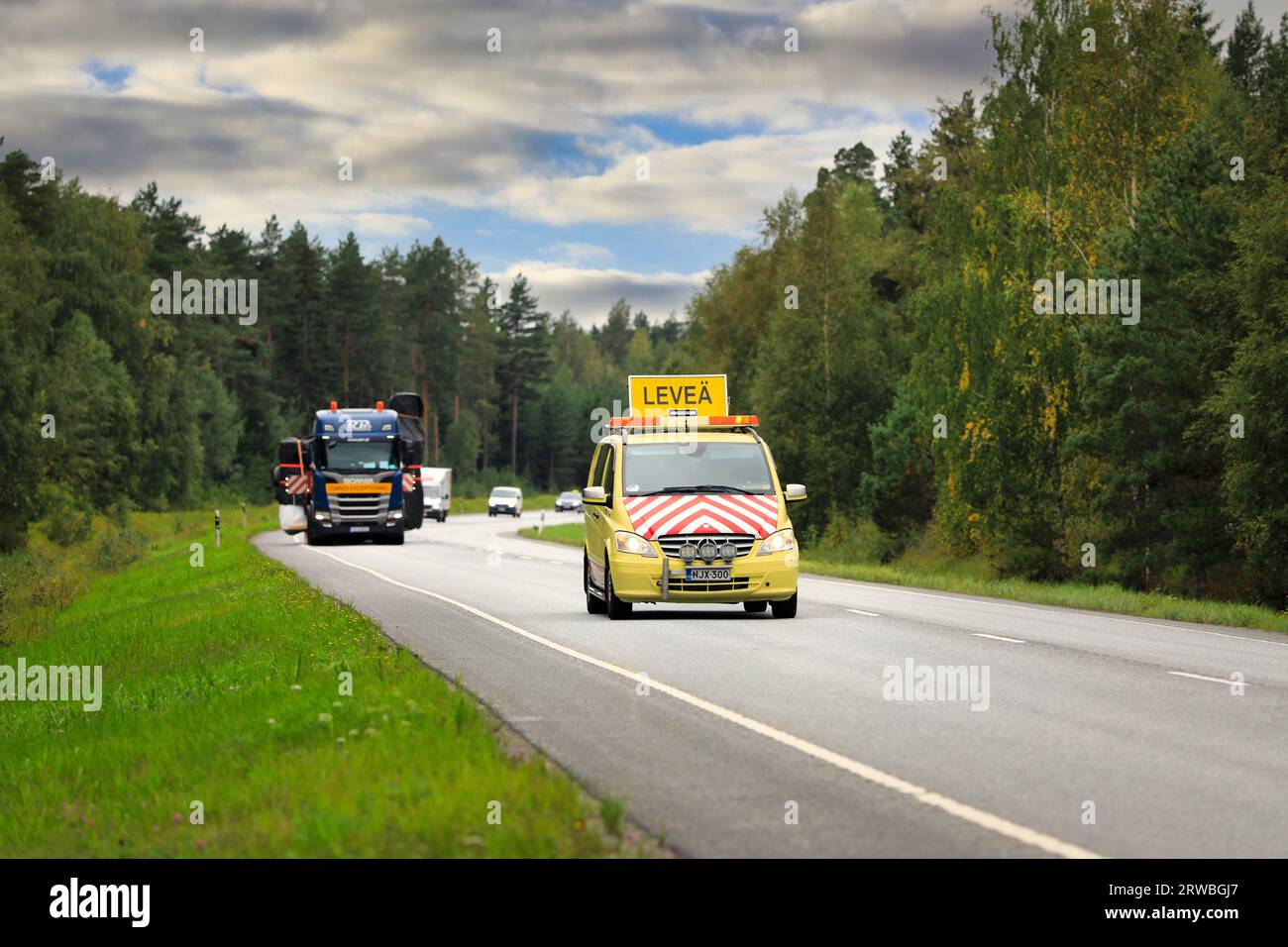 Mercedes-Benz Pilot-Fahrzeug führt im Straßenverkehr Wide Load Transport durch, gezogen von einem Scania Tieflader-Anhänger. Raasepori, Finnland. September 2023. Stockfoto