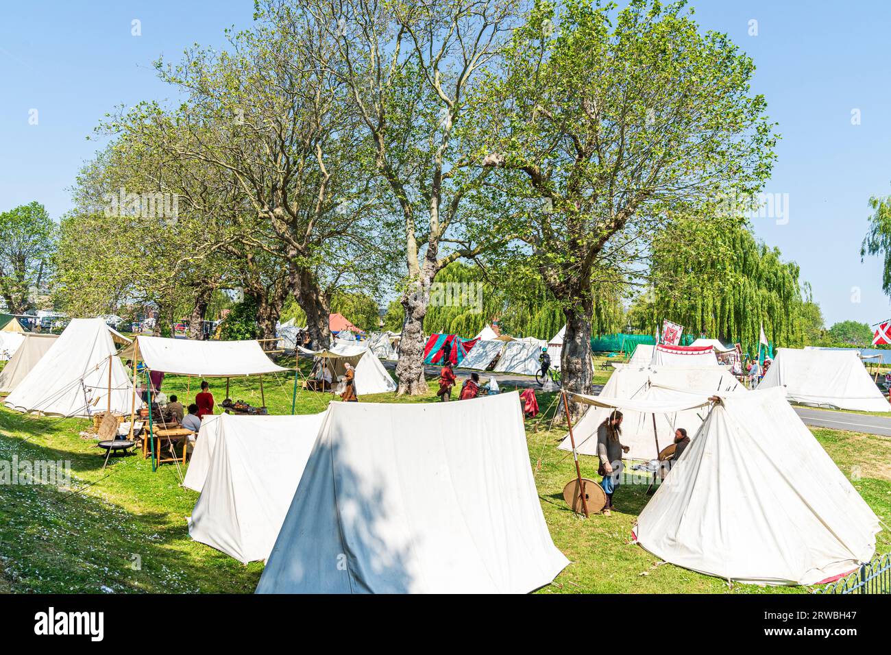 Mittelalterliches Lager für lebendige Geschichte am Flussufer Green in der Stadt Kent in Sandwich. Weiße und farbige Zelte, die unter Bäumen in der Sonne aufgestellt werden. Stockfoto