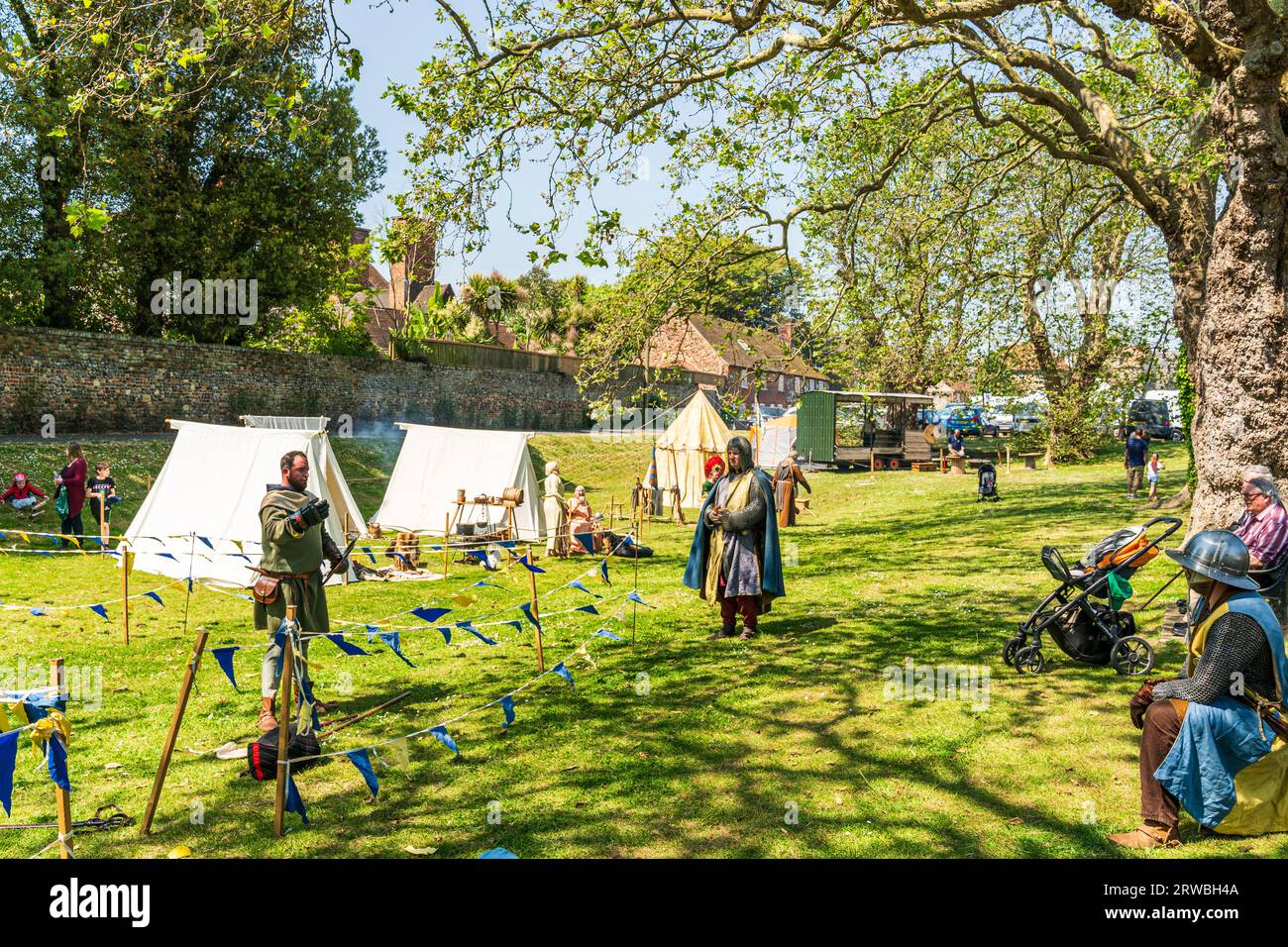 Mittelalterliches Lager für lebendige Geschichte am Flussufer Green in der Stadt Kent in Sandwich. Weiße und farbige Zelte, die unter Bäumen in der Sonne aufgestellt werden. Stockfoto
