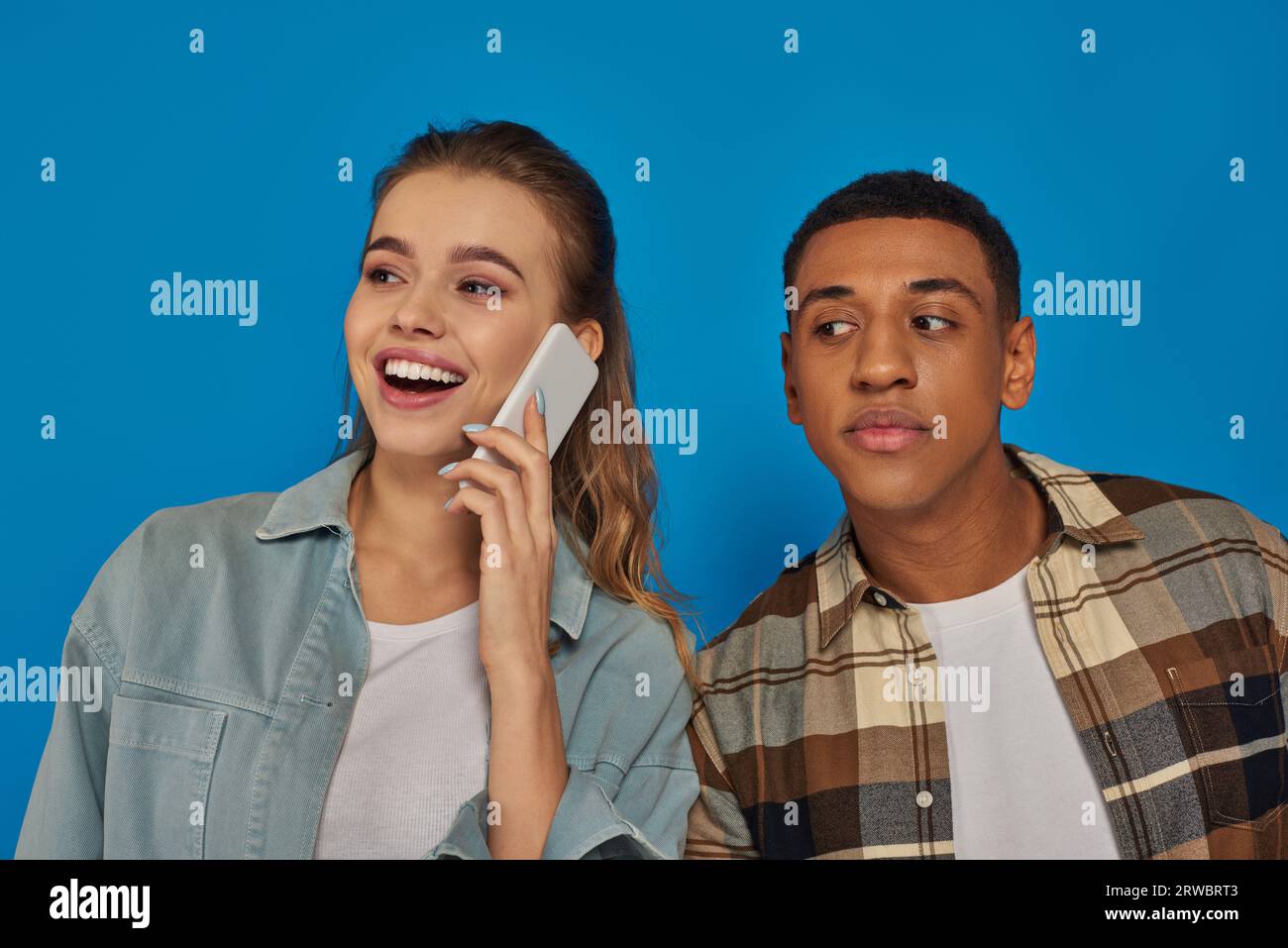 afroamerikanischer Mann, der das Gespräch einer glücklichen Frau hört, die auf dem Smartphone auf blauem Hintergrund spricht Stockfoto