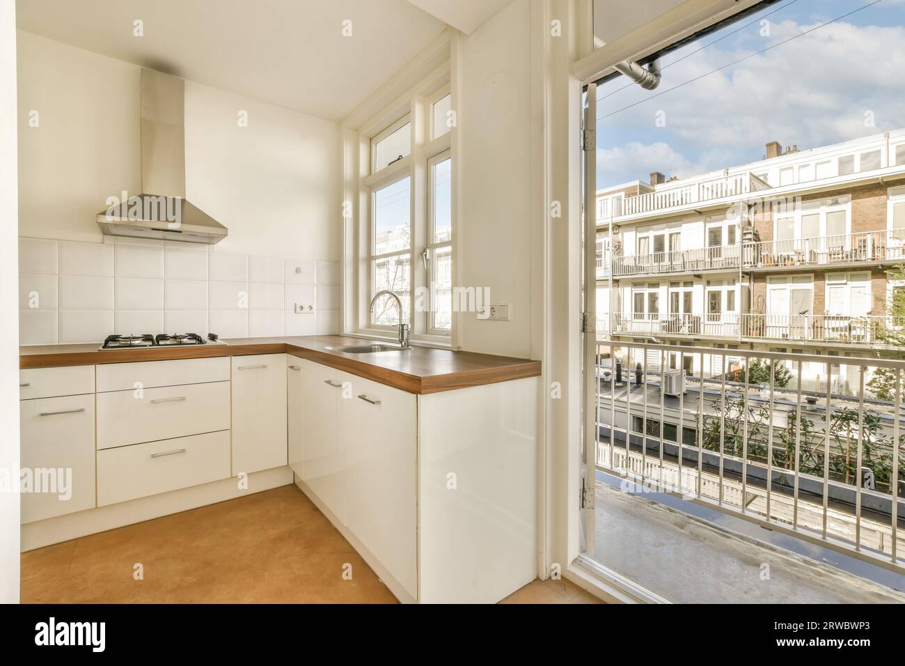 Holztheke mit weißem Schrank und Waschbecken neben großen offenen Fenstern in der modernen Küche des renovierten Apartments Stockfoto