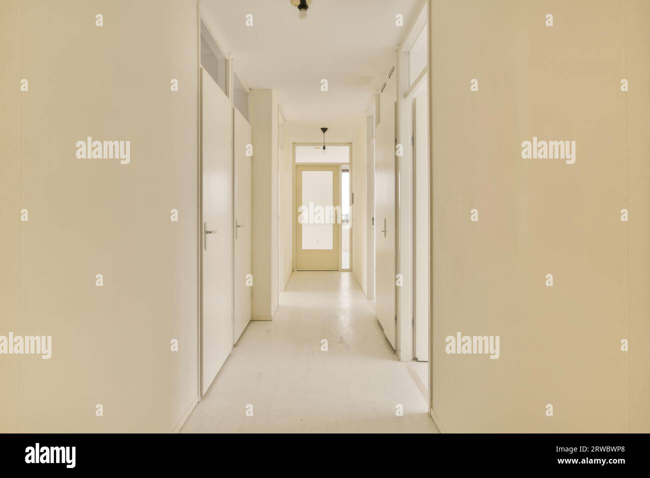Das Innere des langen schmalen Korridors führt zu mehreren Zimmern mit weißen Türen in einem modernen Haus mit beigefarbenen Wänden und laminiertem Boden Stockfoto