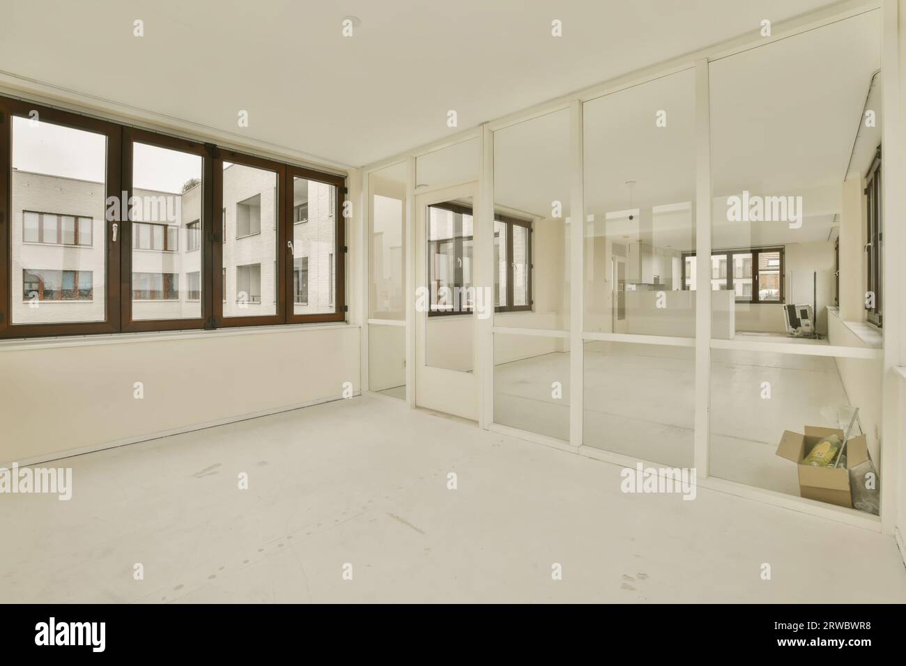 Das geräumige, renovierte Apartment verfügt über große Fenster und Glaswände zwischen leeren Zimmern mit weißen Wänden und Böden Stockfoto