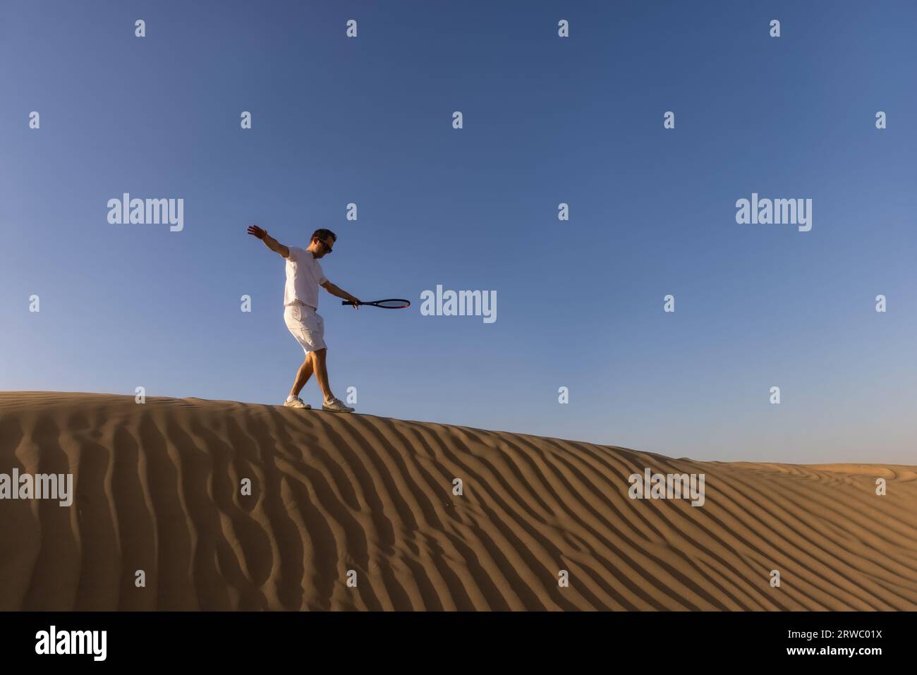 Gutaussehender Mann, der Tennis auf einem Barkhan in der Wüste spielt. Sonnenuntergang. Sport. Gerichte. Hochwertige Fotos Stockfoto