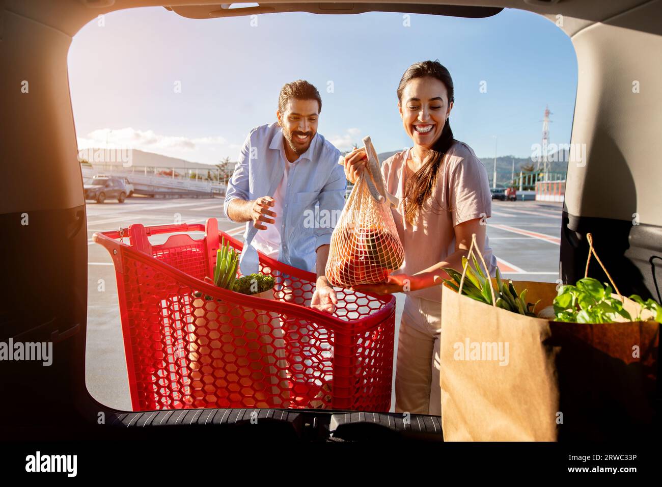 Aufgeregte brasilianische Ehepartner packen Einkaufstaschen mit frischem Essen in den Kofferraum, Blick vom Fahrzeuginnenraum Stockfoto