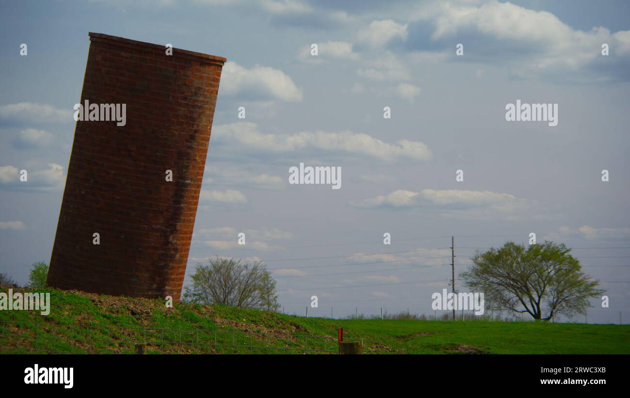 Das geneigte Getreidesilo trotzt der Physik, während es auf einem bewirtschafteten und charmanten Bauernhof in Iowa gegen die Schwerkraft kämpft. Stockfoto