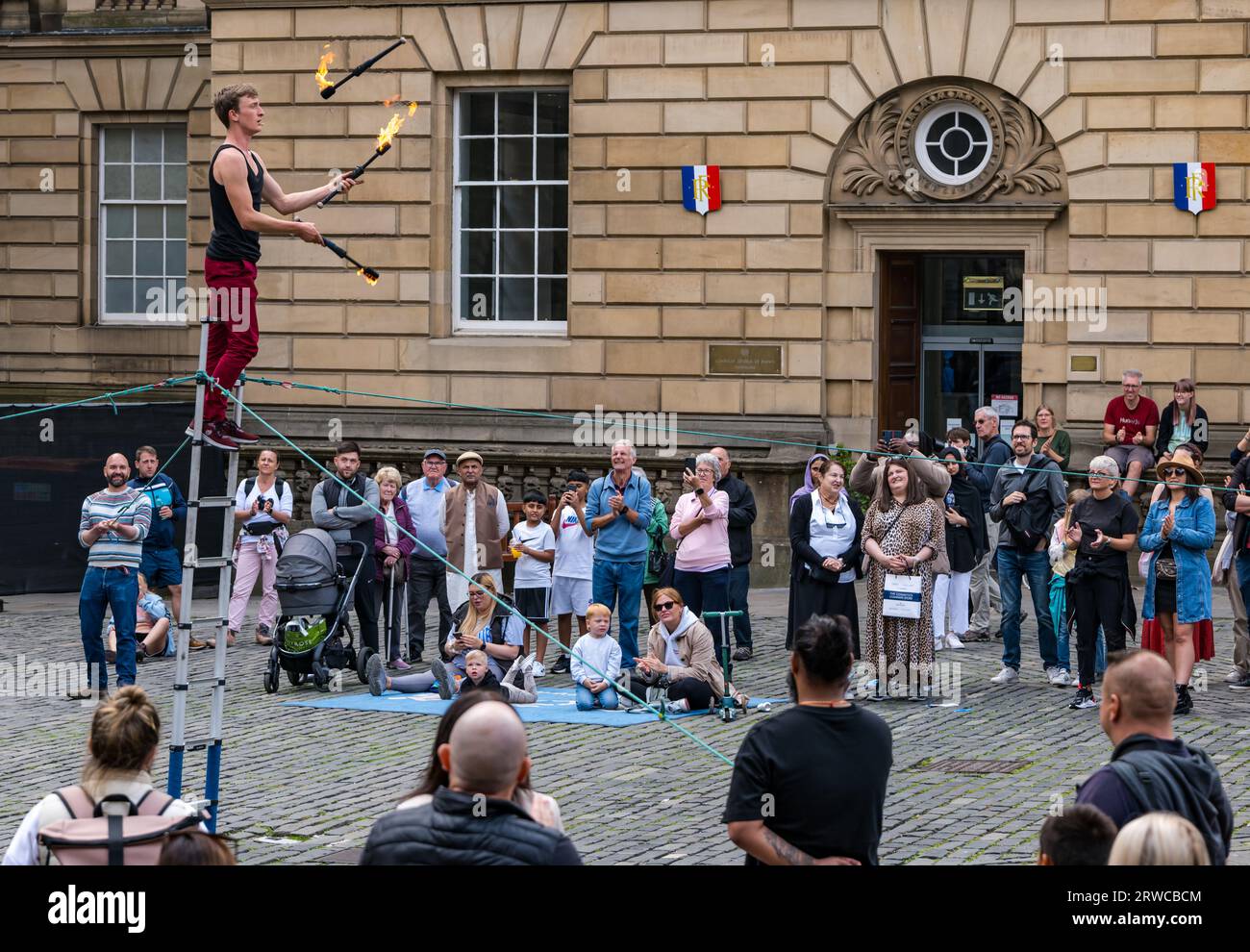 Straßenkünstler, der mit Feuerfackeln jongliert, während er auf einer Leiter steht, Edinburgh Festival Fringe, Parliament Square, Schottland, Großbritannien Stockfoto