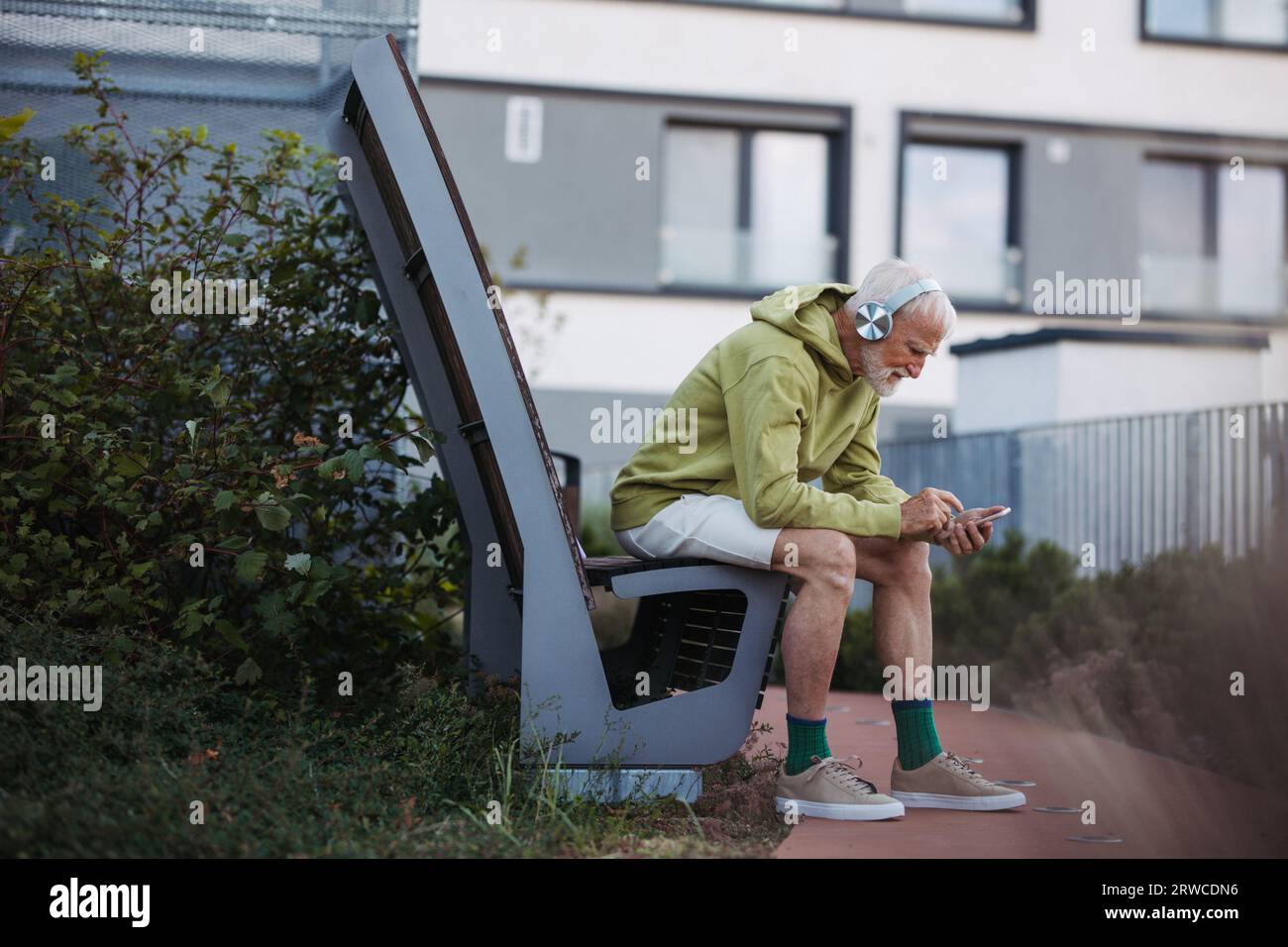 Älterer Mann, der Musik über kabellose Kopfhörer hört und sich auf seinen Morgenlauf vorbereitet. Stockfoto