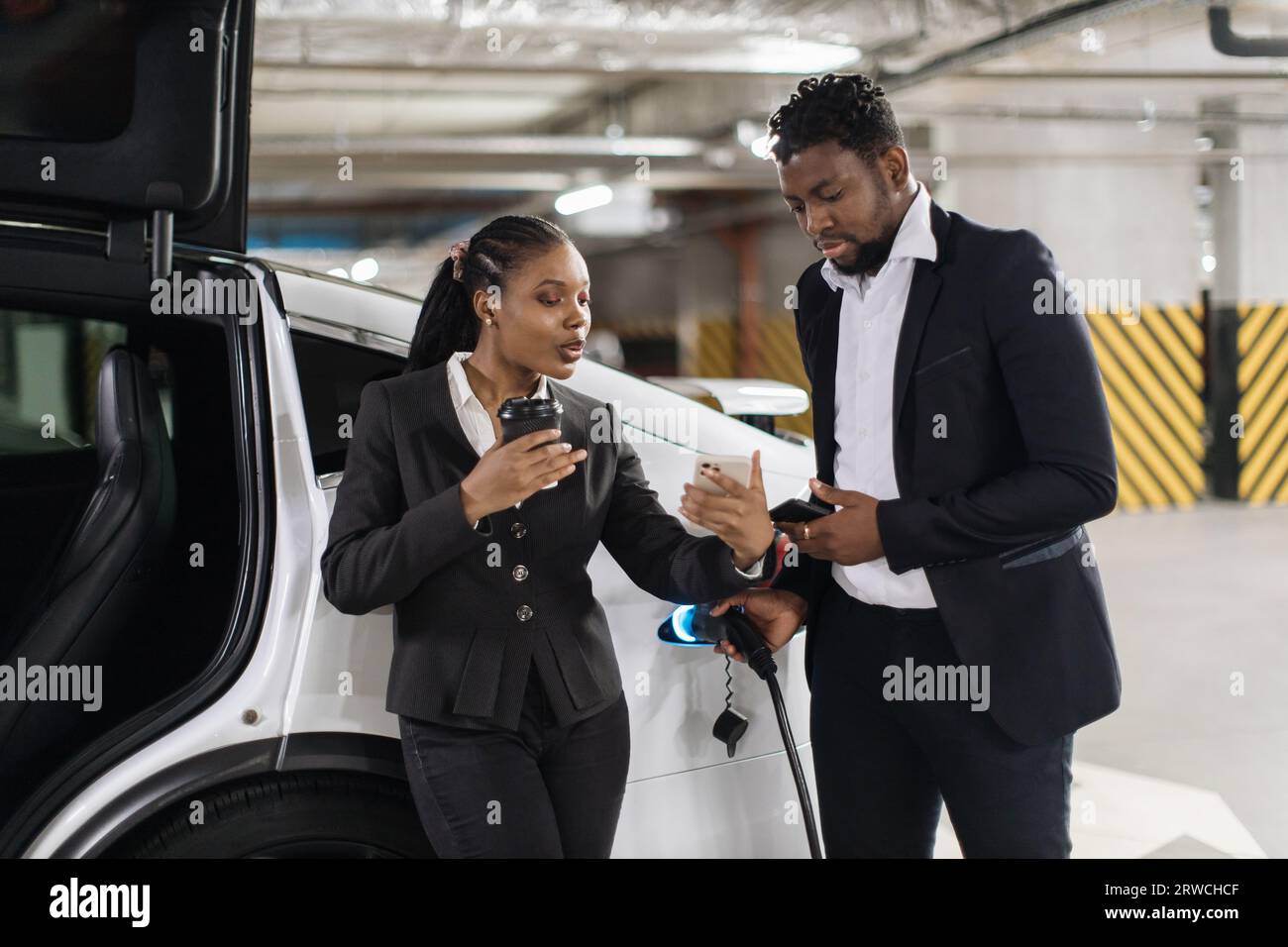 Kollegen, die beim Auffüllen des Elektroautos einen Screenshot ansehen Stockfoto