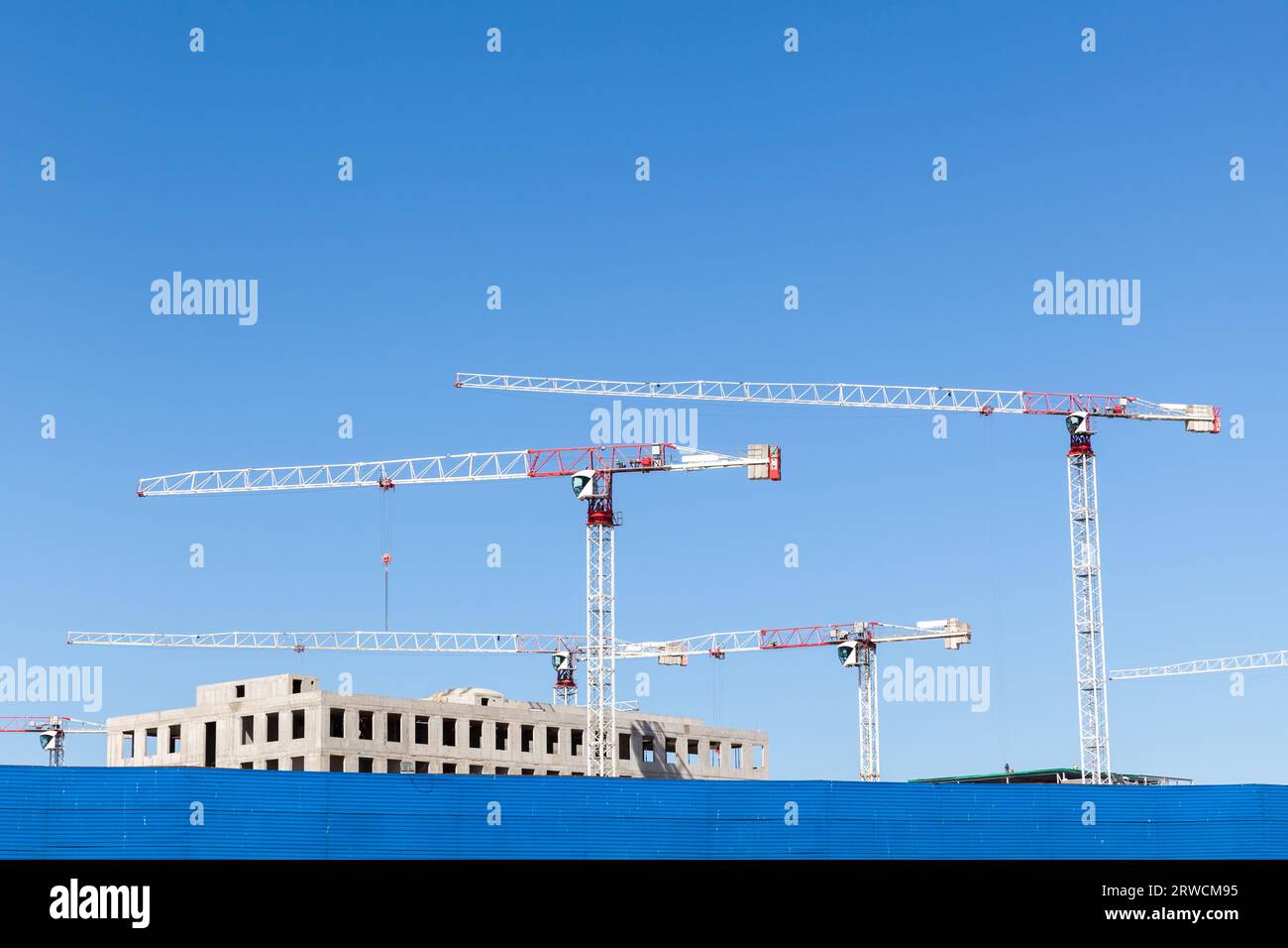 Baustelle mit weißen Turmdrehkranen unter klarem blauen Himmel Stockfoto