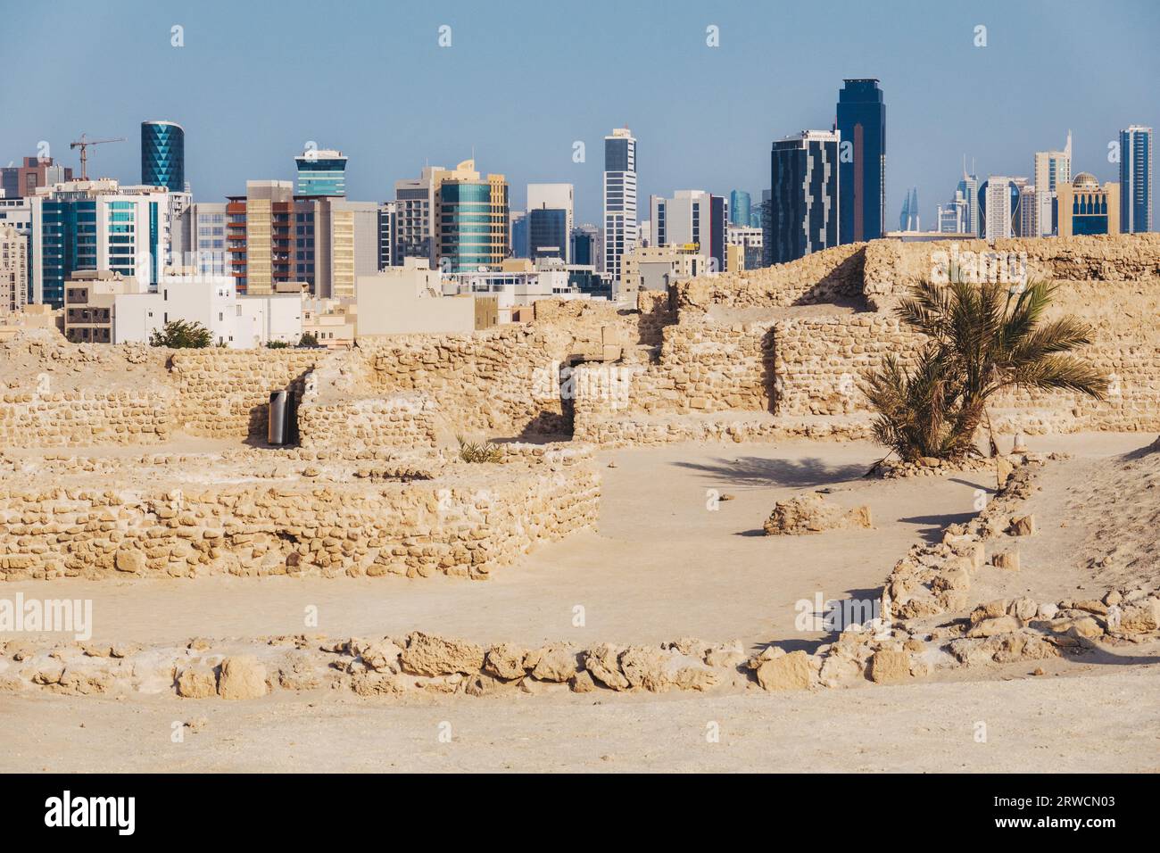 Alt und neu: Die Ruinen von Bahrain Fort, das 2300 v. Chr. datiert, gegenüber der modernen Skyline der Innenstadt von Manama Stockfoto
