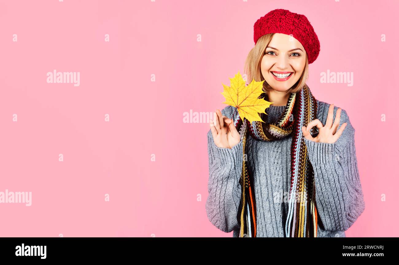 Lächelnde Frau in warmen Kleidern mit Ahornblatt, das eine gute Geste zeigt. Schönes Mädchen in Strickpullover, Schal und rotem französischem Berret mit perfektem Schild Stockfoto