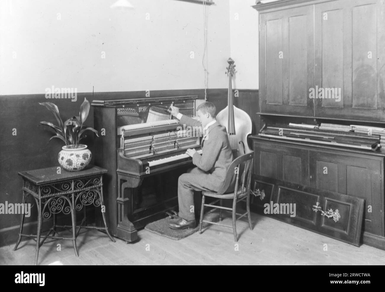 Ein blinder Mann, der ein aufrechtes Klavier stimmt, mit einem Cello in der Ecke auf seiner rechten Seite. September 1912. Fotograf unbekannt. Stockfoto