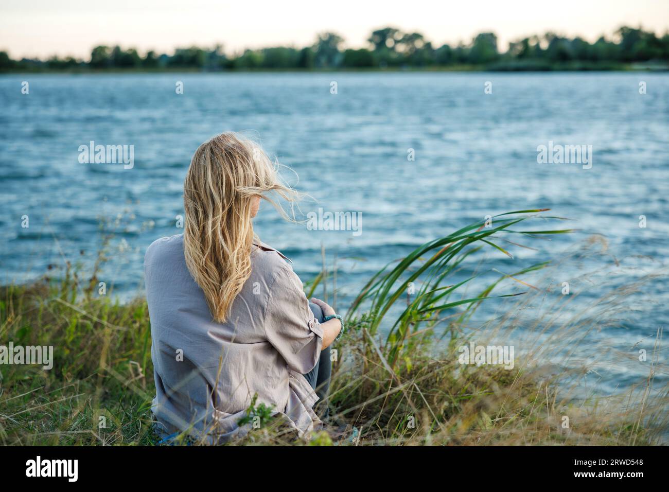Frau entspannt sich in der Natur am See, um ihre Achtsamkeit und psychische Gesundheit zu verbessern. Genießen Sie frische Luft und digitale Entgiftung im Freien Stockfoto