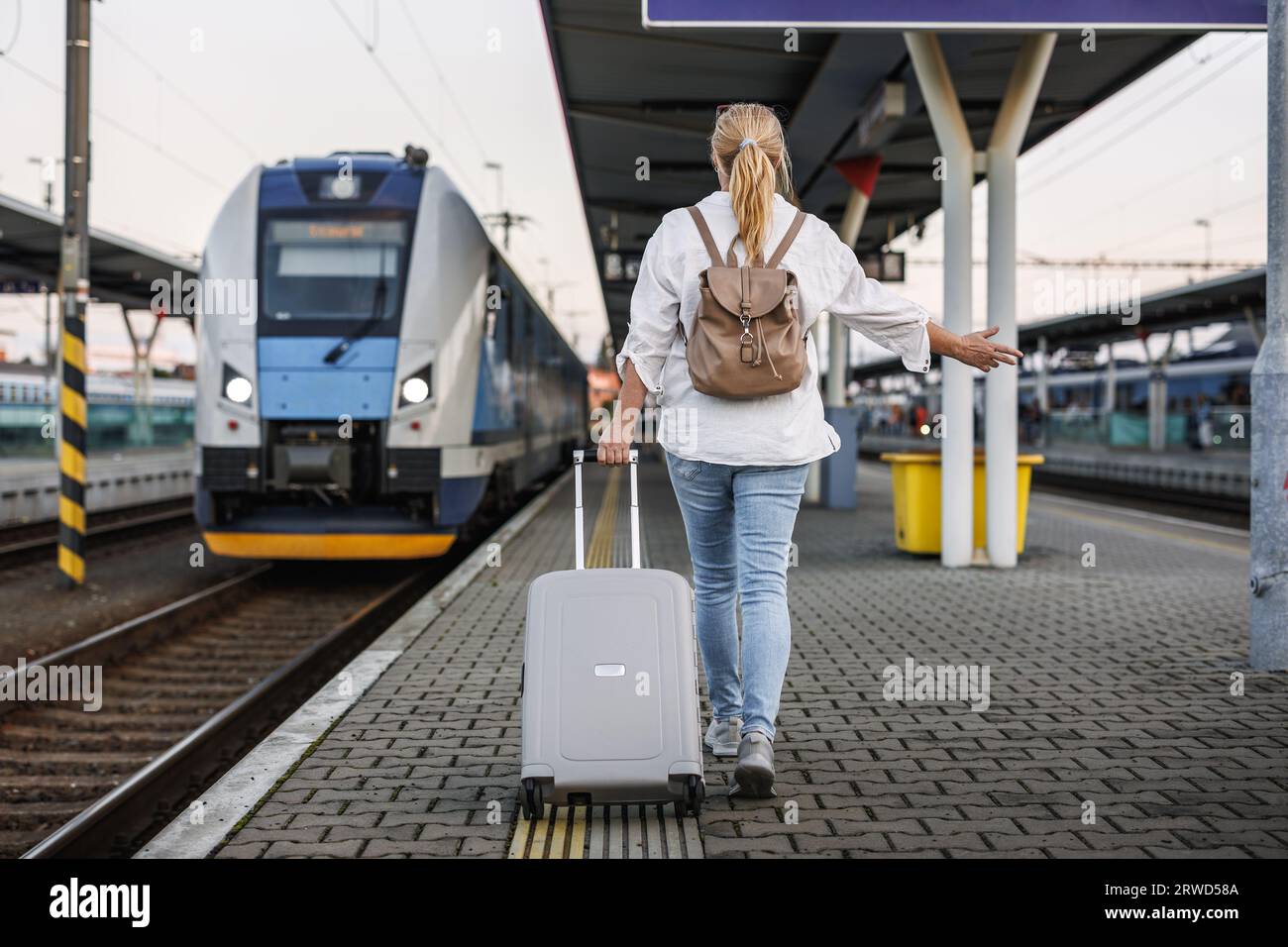 Frau, die mit dem Zug reist. Weibliche Touristin mit Koffer in Eile am Bahnsteig. Reise-Lifestyle Stockfoto