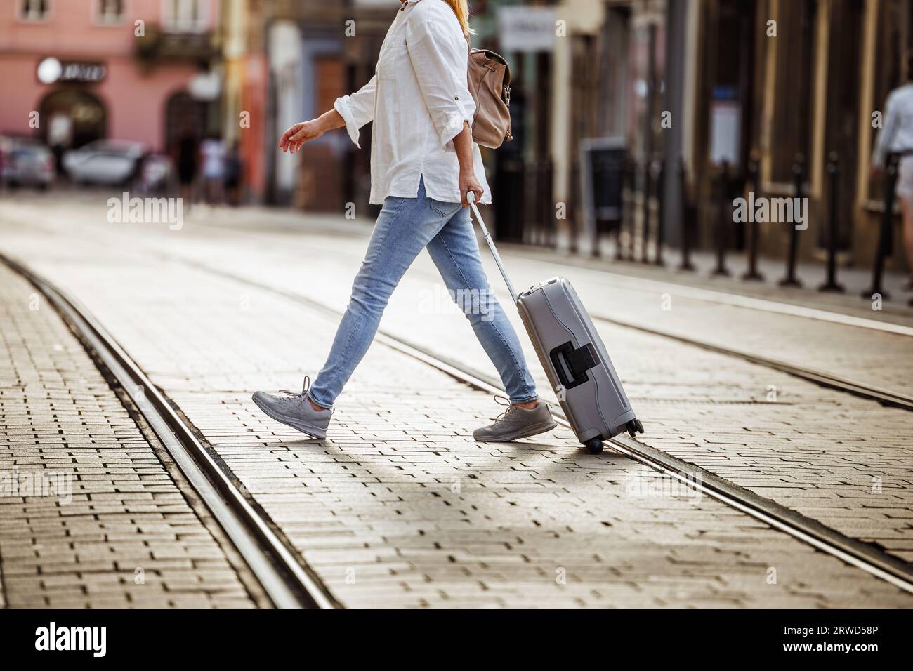 Eine Touristin mit Koffer geht über die Straße mit Straßenbahnschienen in der Stadt. Reise- und Urlaubslifestyle Stockfoto