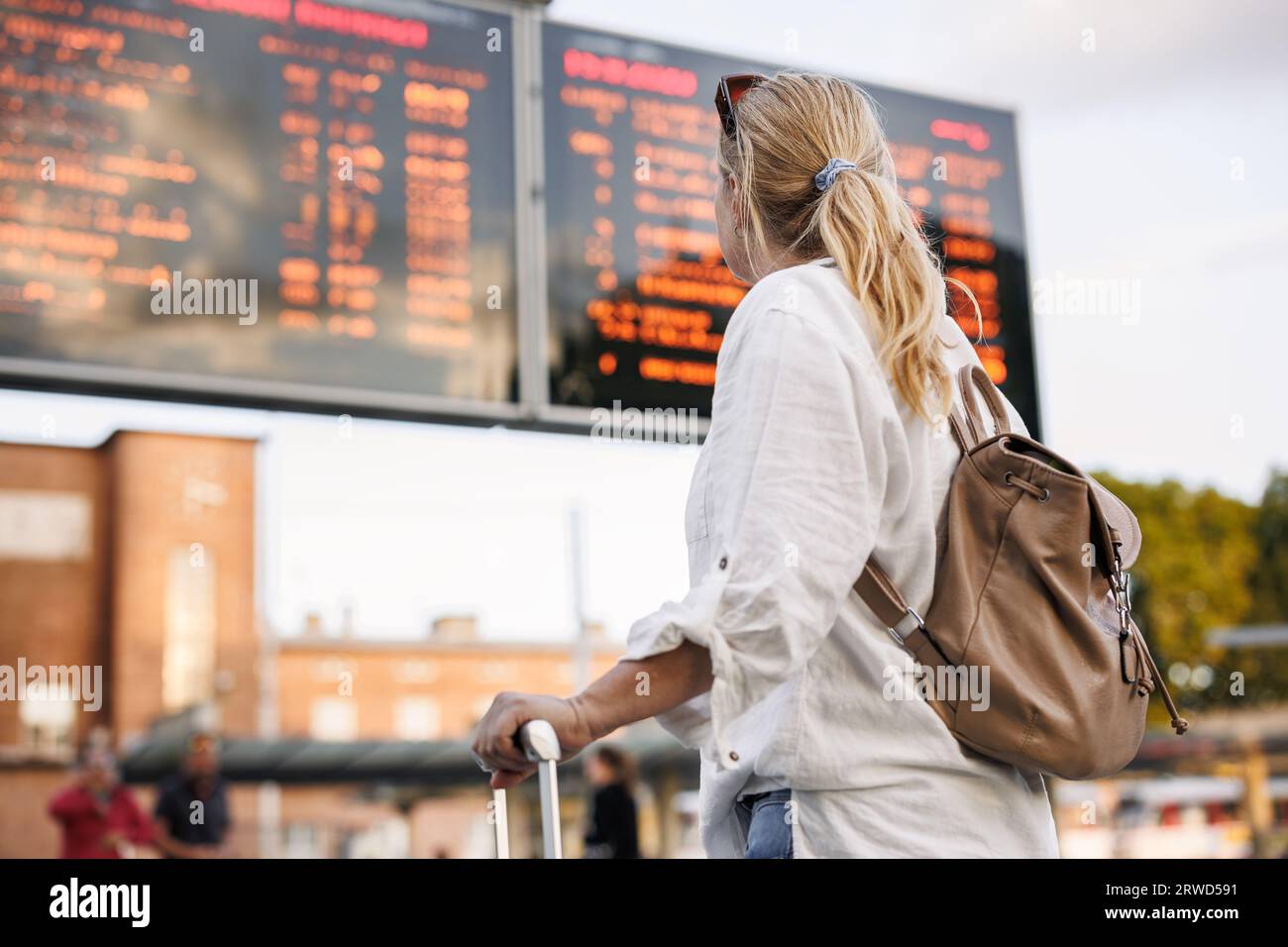 Die Passagierin mit Rucksack überprüft den Zeitplan für Ankunft und Abflug am Bahnhof oder Busbahnhof. Reisen Sie in den Urlaub Stockfoto