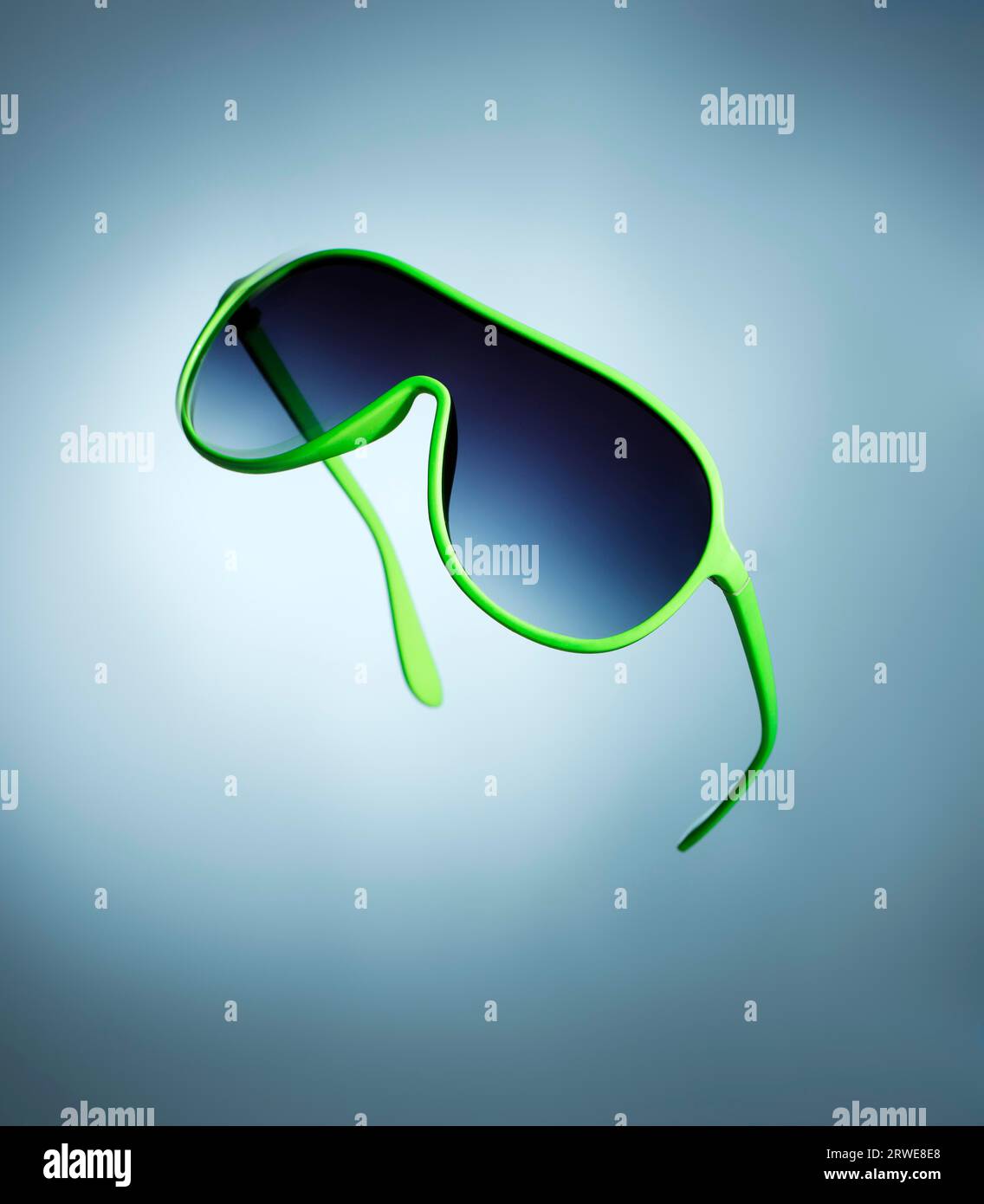 Günstige grüne 1980er Jahre Kunststoff-Sonnenbrille auf blauem Hintergrund Stockfoto