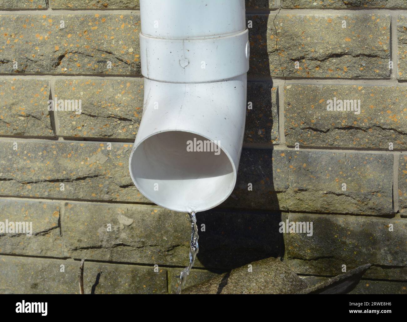 Weiße Kunststoff-Regenrinne das downspout-Rohr läuft in der Nähe der Hausgründungswand aus Regenwasser. Regenwasser fließt aus der Dachrinne Stockfoto