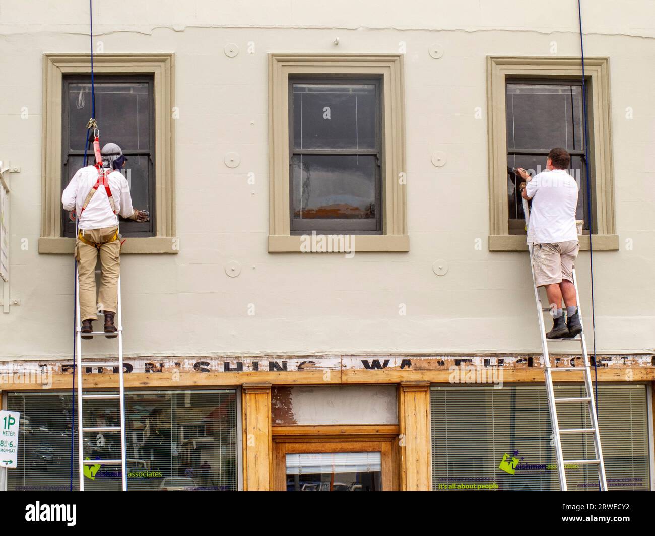 Maler auf Leitern malen die Fensterrahmen eines historischen georgianischen Shopfront in Melville Street, Hobart, Tasmanien. Aus Sicht der Gesundheit und Sicherheit trägt man einen Sicherheitsgurt, der andere nicht. Stockfoto