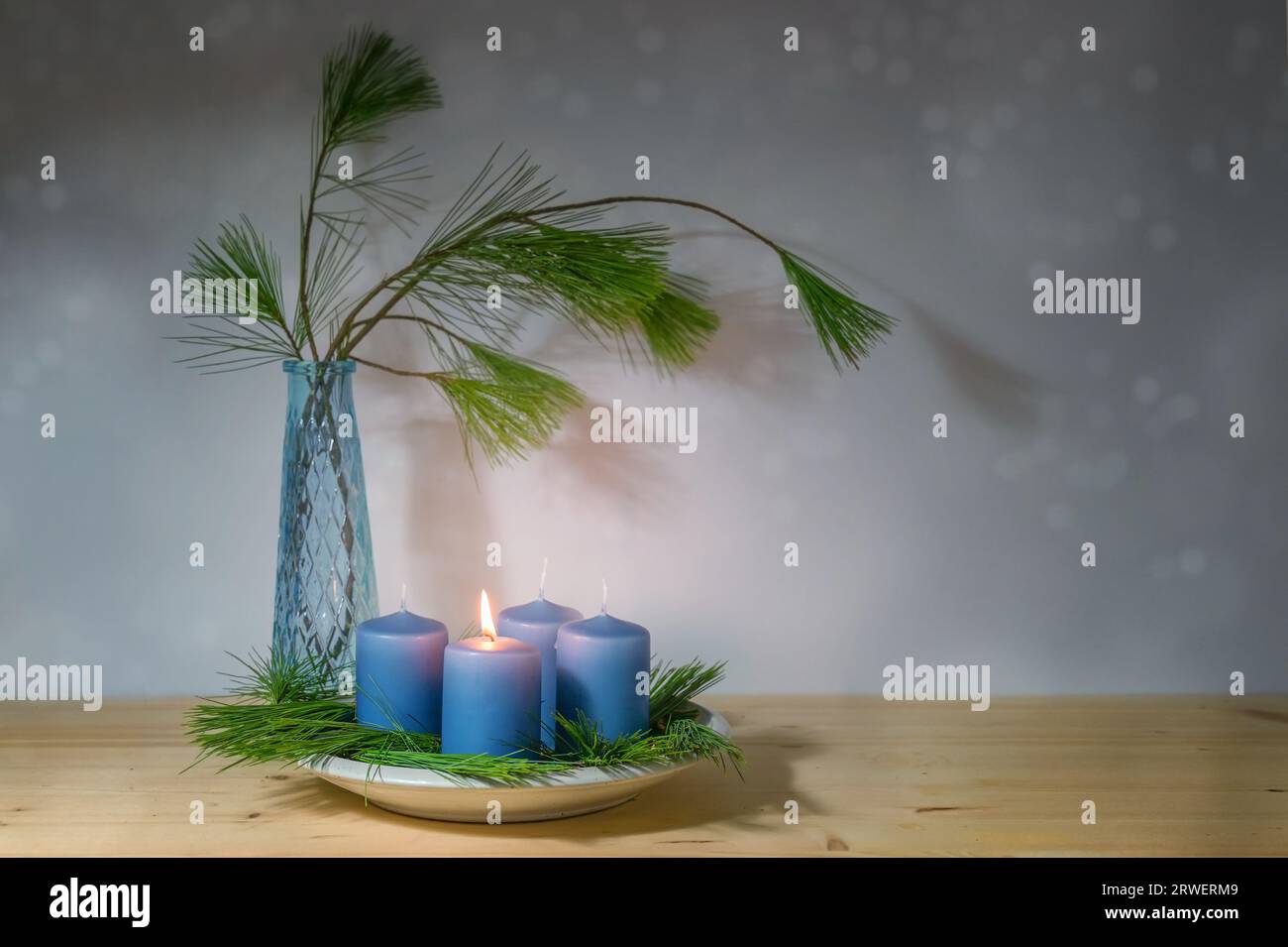 Blaue Kerzen, eine wird für den ersten Advent angezündet, und eine Vase mit Kiefernzweigen, moderne Dekoration in der Weihnachtszeit, Kopierraum, ausgewählter Fokus, n Stockfoto