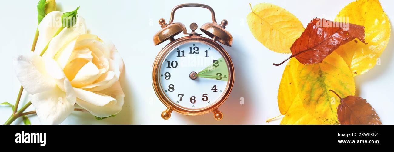 Vintage-Wecker, der die Stunde zwischen Sommerzeit und Herbst anzeigt, symbolisiert durch eine Rose auf der einen Seite und Herbstlaub auf der OT Stockfoto