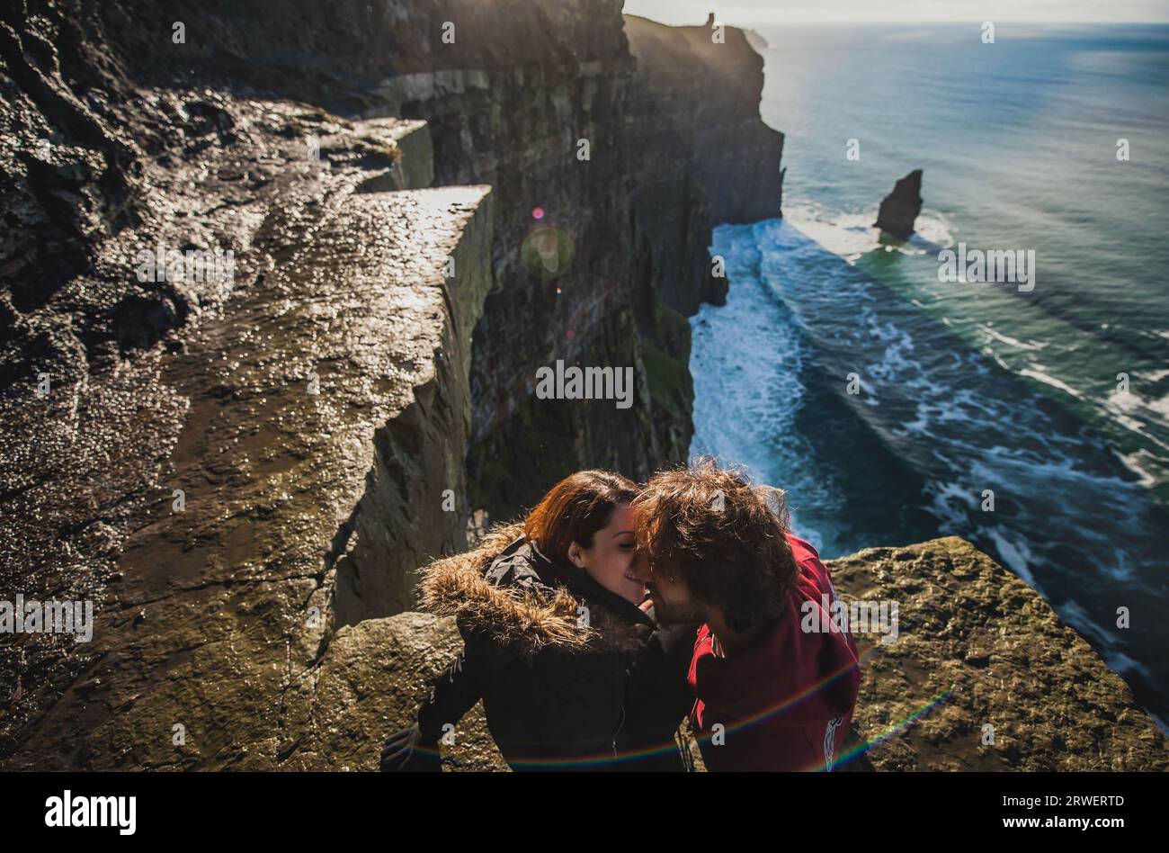 Ein paar männliche und weibliche Scherze am Rande einer hohen Klippe. Mann und Frau küssen und lieben auf einem Abenteuer und romantischen Ausflug am Wasser Stockfoto