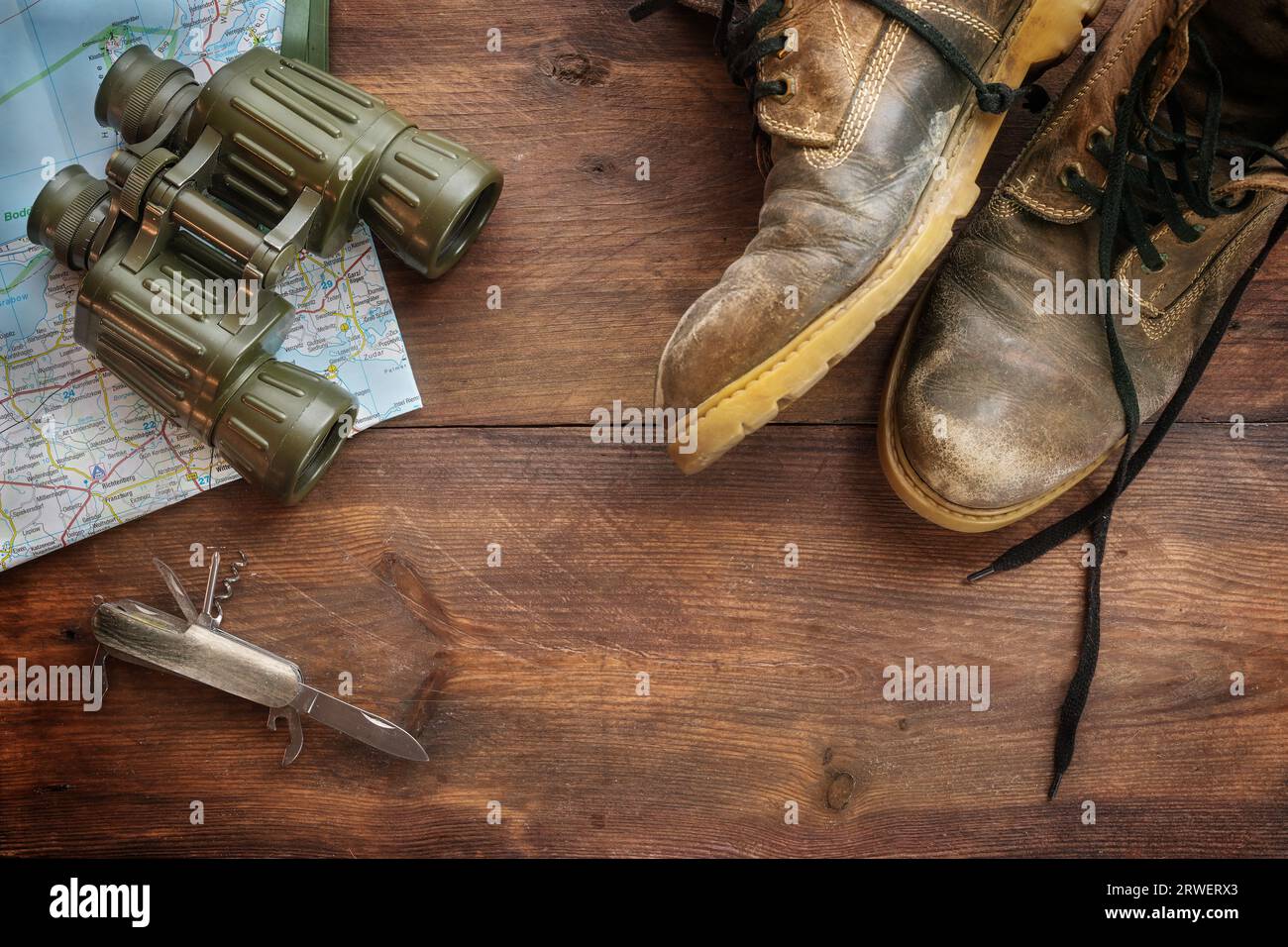 Alte Lederstiefel, Fernglas, Karte und Taschenmesser auf dunklem rustikalem Holz, Konzept für Reise-, Wander- und Abenteuerurlaub, Hochwinkel-Blick Stockfoto