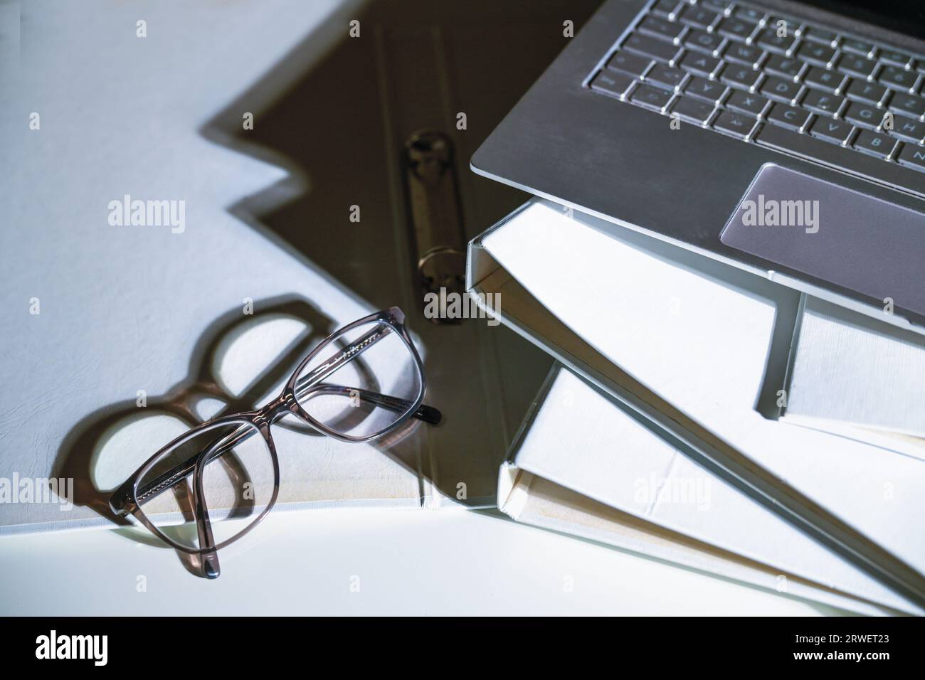 Brillen und ein Teil eines Laptops auf weißen Aktenordnern mit scharfen Schatten auf einem Büroschreibtisch, Geschäftskonzept, Kopierraum, ausgewählter Fokus, schmal d Stockfoto