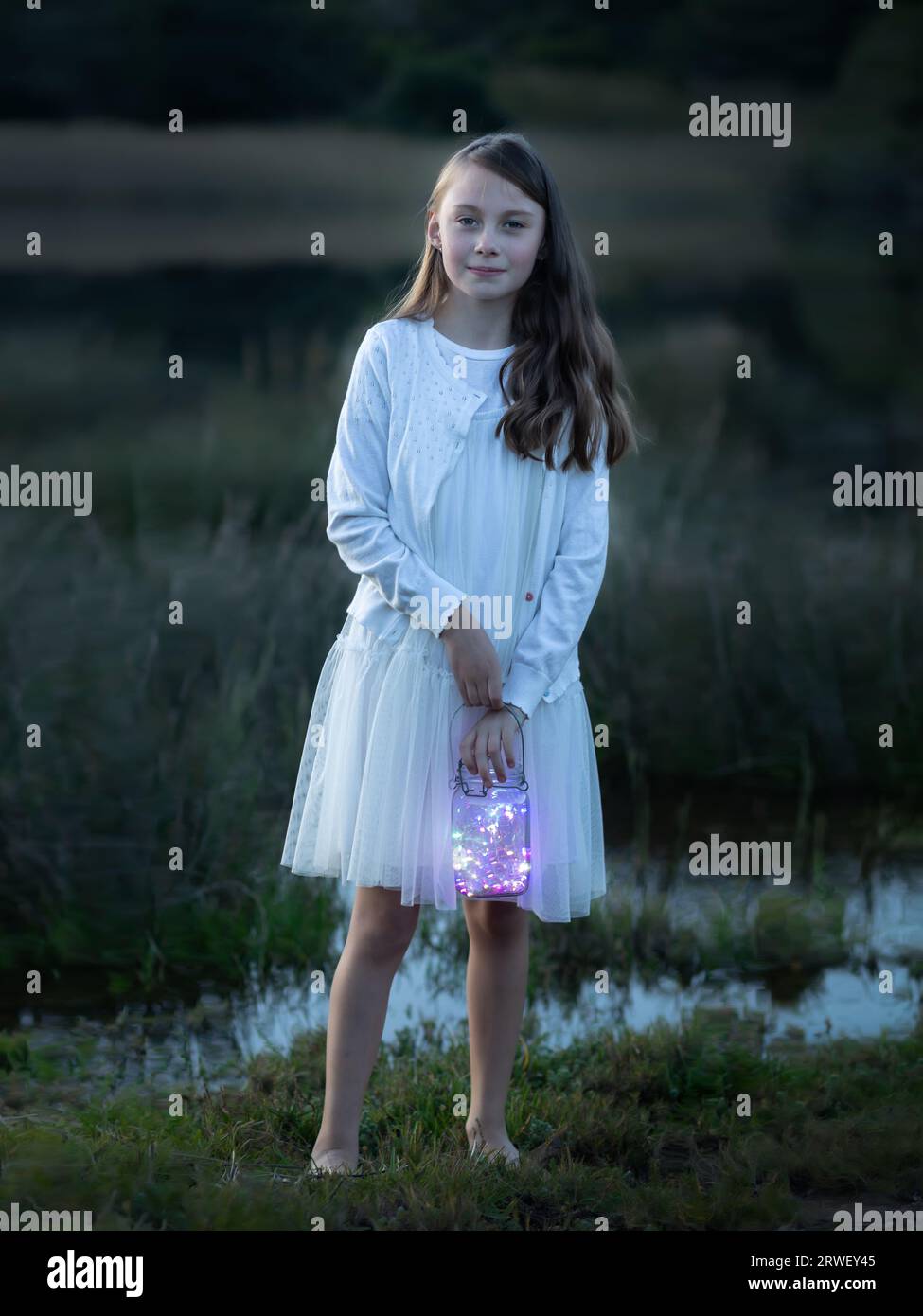 Portrait eines jungen Mädchens in einem weißen Kleid in der Abenddämmerung mit einer Laterne Stockfoto
