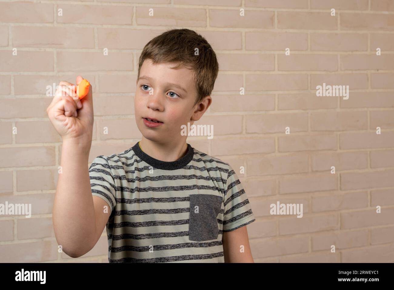 Ein glücklicher weißer Junge im Schulalter schreibt in der Luft mit einem orangefarbenen Marker. Das Konzept von Studium, Schultätigkeit und Bildung Stockfoto