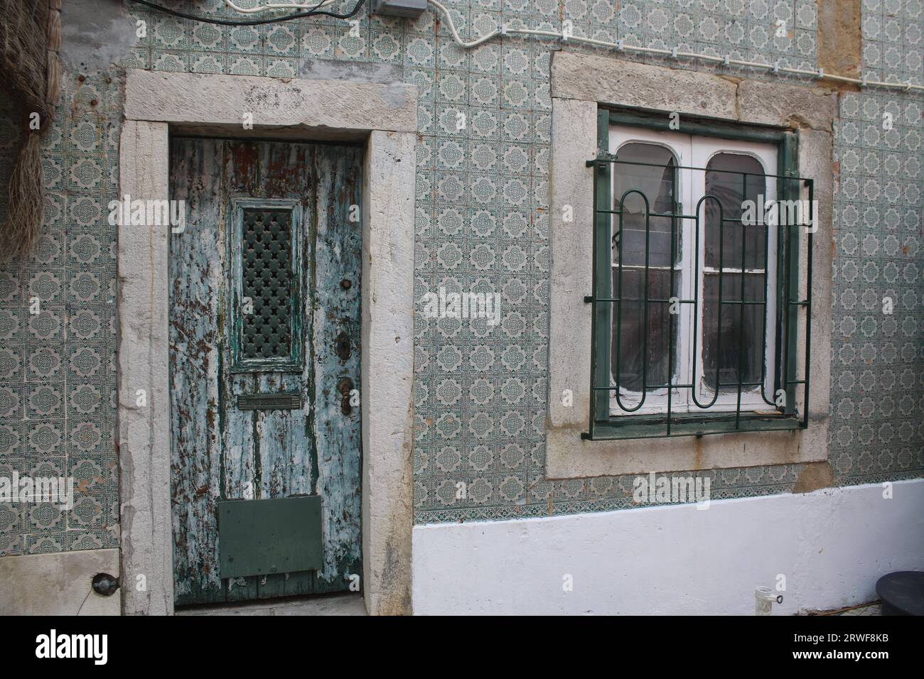 Vordertür in Vintage-Optik mit Lackierung und Metallgrill mit Fenstermuster, umgeben von grün und weiß gemusterten portugiesischen Wandfliesen. Stockfoto