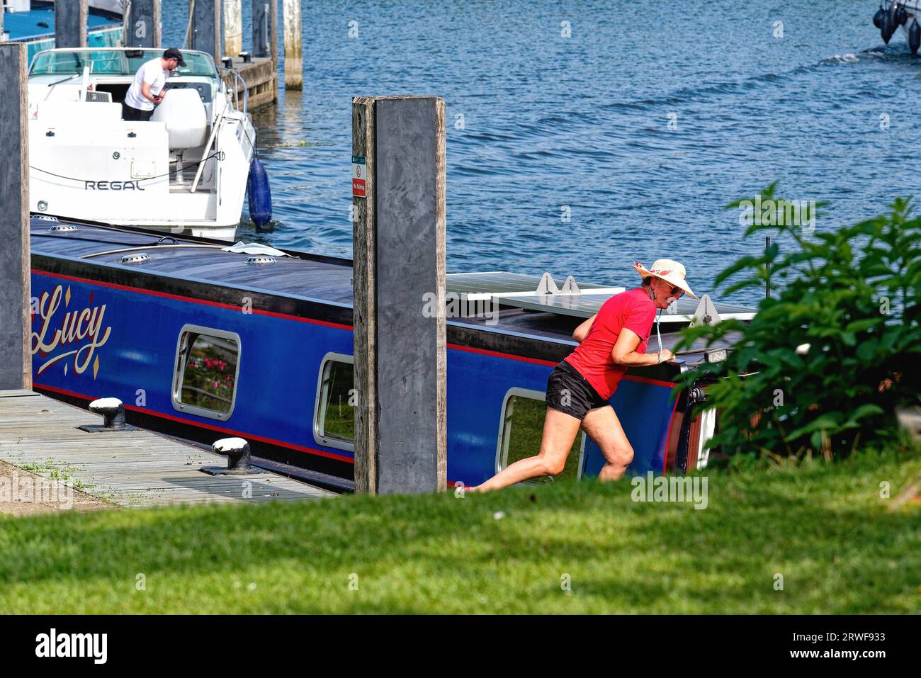 Eine attraktive Frau mittleren Alters in Shorts, Hut und rotem Oberteil, die ein schmales Boot an der Themse im Shepperton Surrey England anlegt Stockfoto