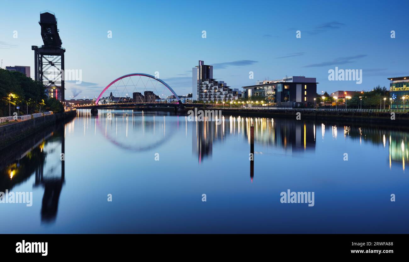 Wunderschöne Clyde Arc Bridge bei Sonnenuntergang über dem Fluss in Glasgow, Schottland, Großbritannien. Es ist schönes Wetter mit Reflexionen auf dem Wasser, blauer Himmel, Lichter von Gebäuden Stockfoto