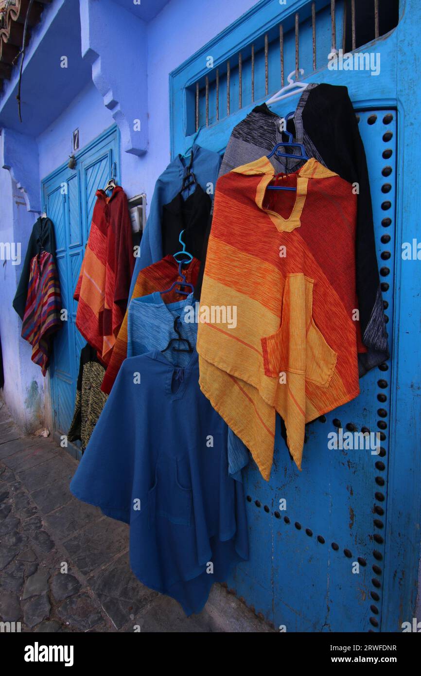 In einer blau bemalten Gasse in Chefchaouen, auch bekannt als Blue City oder Blue Pearl's Souk, werden vielfarbige ethnische marokkanische Mäntel, Djellabas, verkauft. Stockfoto