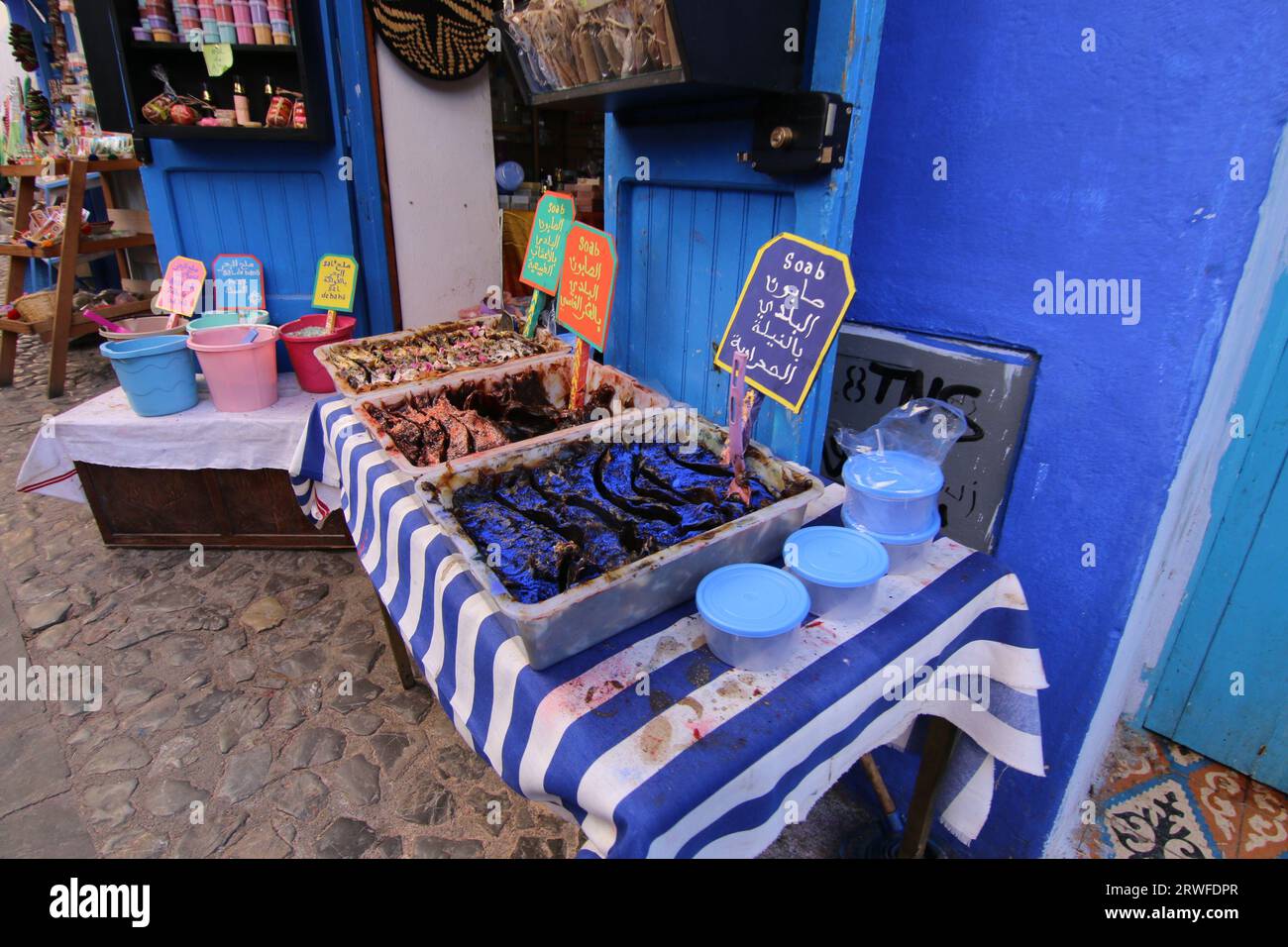 Eine lebendige, farbenfrohe Szene im Chefchaouen Souk mit dekorativer marokkanischer schwarzer Seife in Tabletts auf einem blau-weiß gestreiften Tuch und anderen Souvenirs zum Verkauf Stockfoto