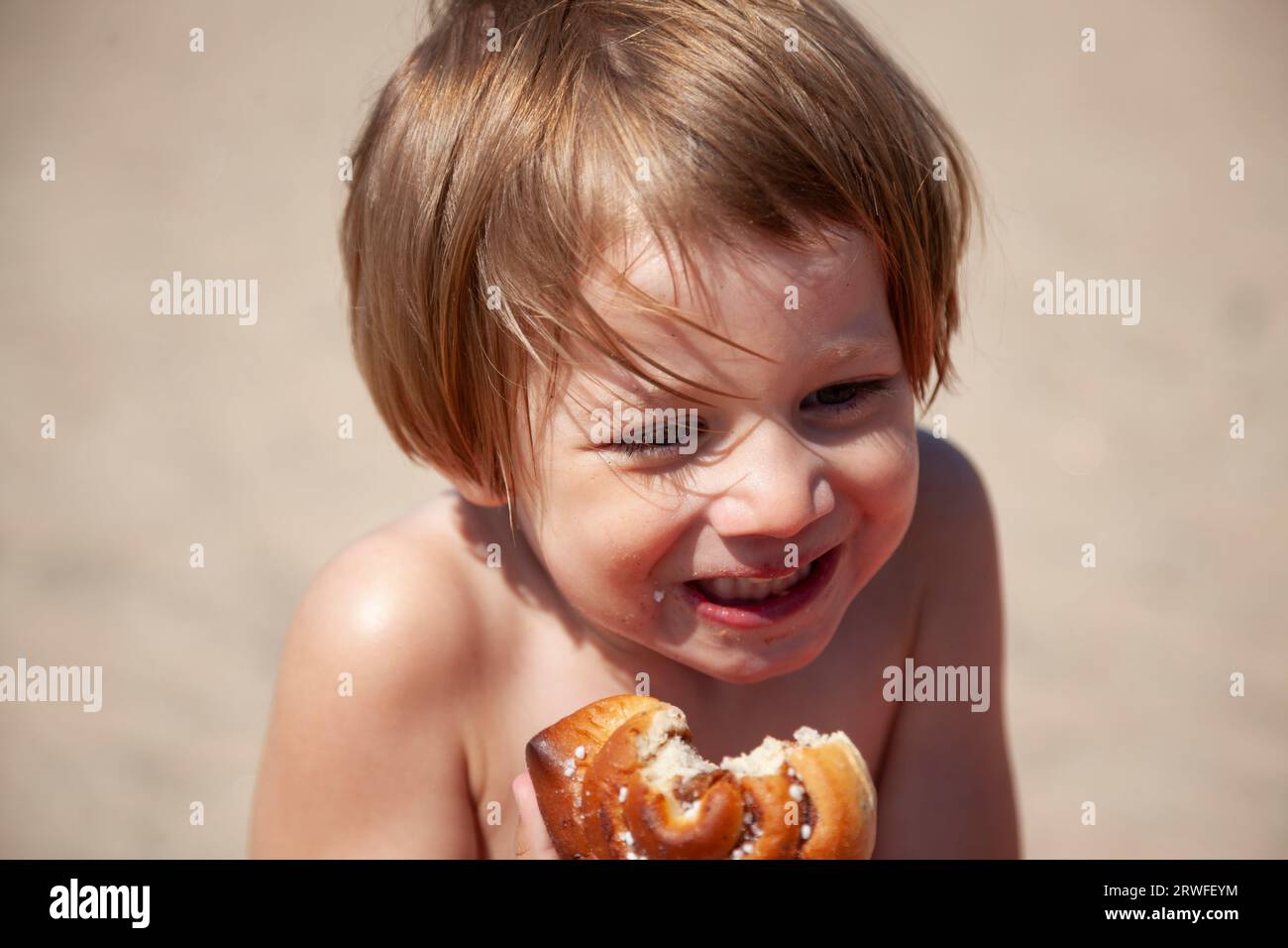 Umea, Schweden - 11. Juli 2023: Kleines Mädchen isst Brötchen am Sandstrand Stockfoto