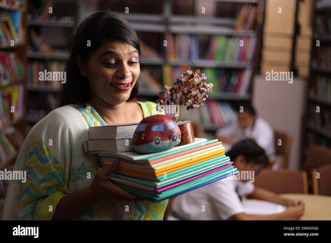 Indische Lehrerin hält ein Bündel Bücher in der Hand, steht in der Bibliothek, studiert Druck, erzieherische Kraft. Stockfoto