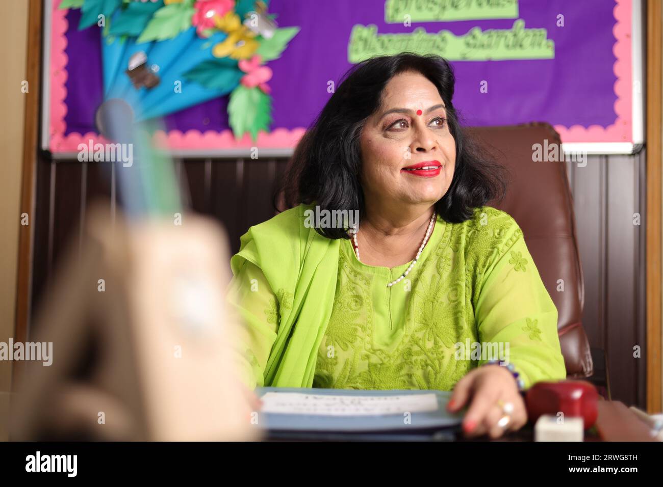 Schulleiterin, glücklich sitzend, stolz auf die Schüler ihrer Schule, lächelnd. Stockfoto