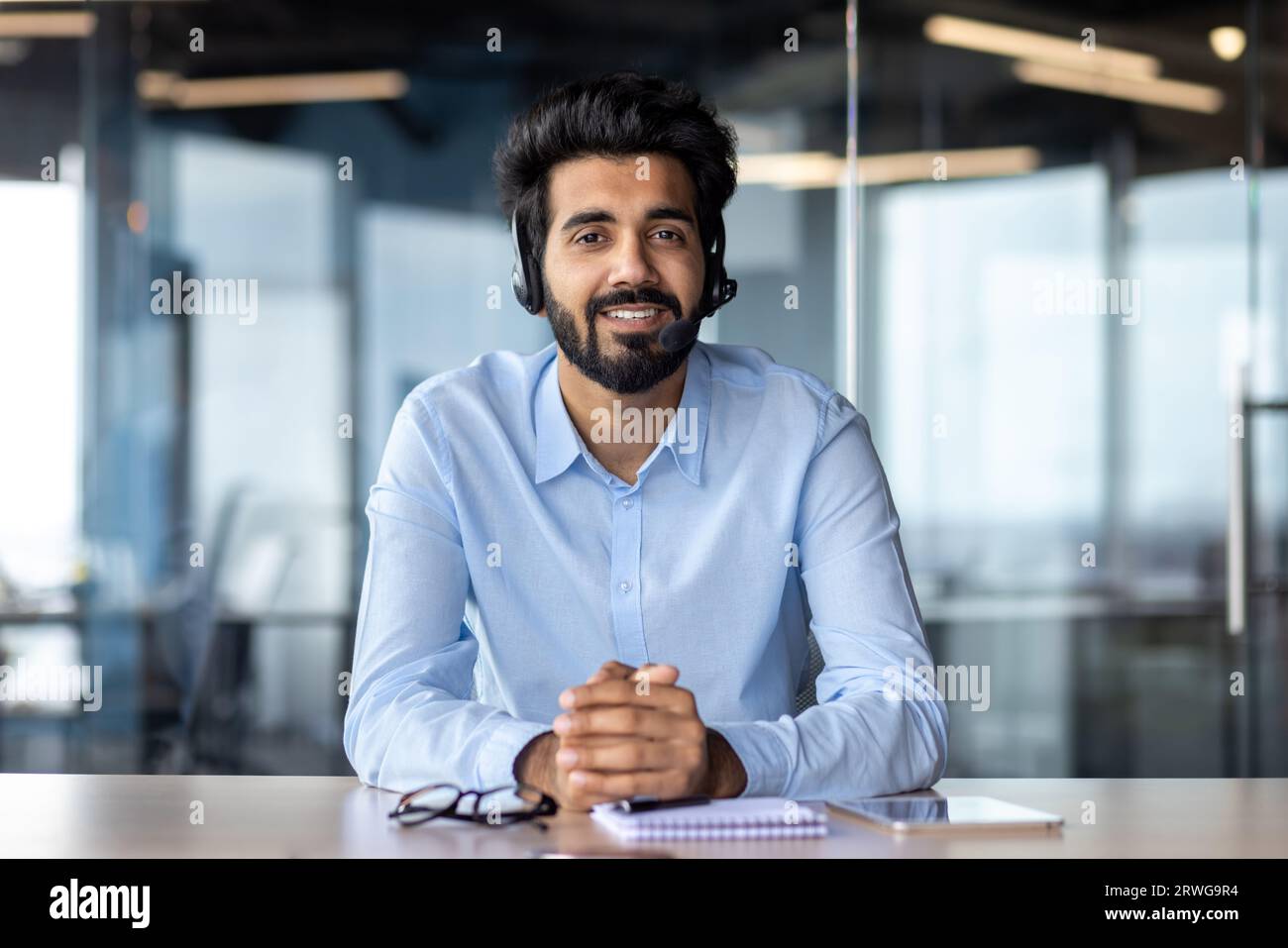 Porträt eines jungen indischen Lehrers in einem Headset, der vor der Kamera im Büro sitzt und online spricht. Stockfoto