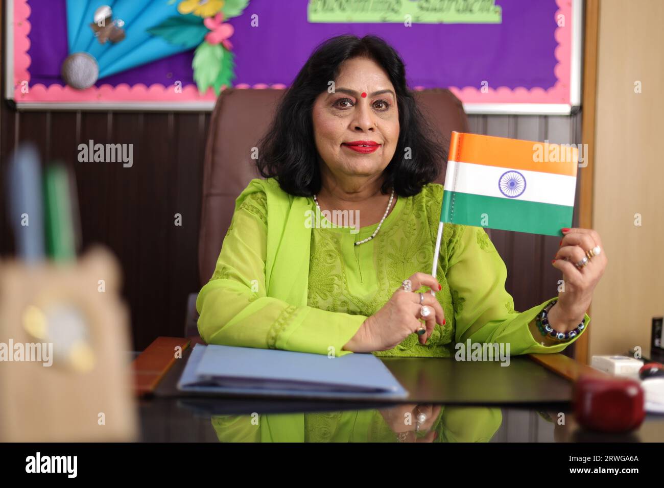 Stolzer Schuldirektor, der die indische Flagge zeigt, sitzt selbstbewusst in ihrem Büro. In die Kamera schauen. Stockfoto