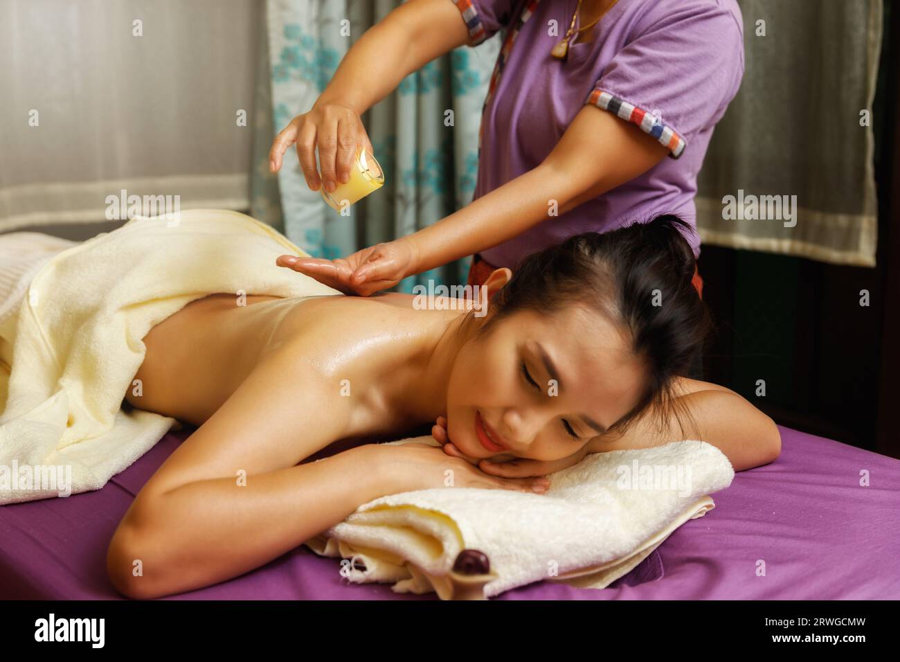 Masseuse tropft warmes Massageöl von einer Kerze auf den Rücken der jungen Frau. Stockfoto