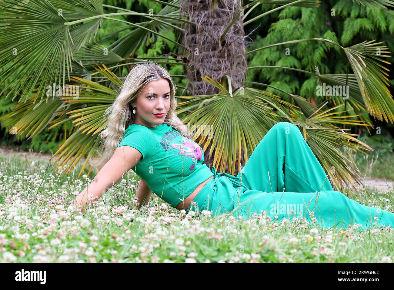 Blonde Frau mit langen Haaren und grünem Outfit posiert in der Natur Stockfoto