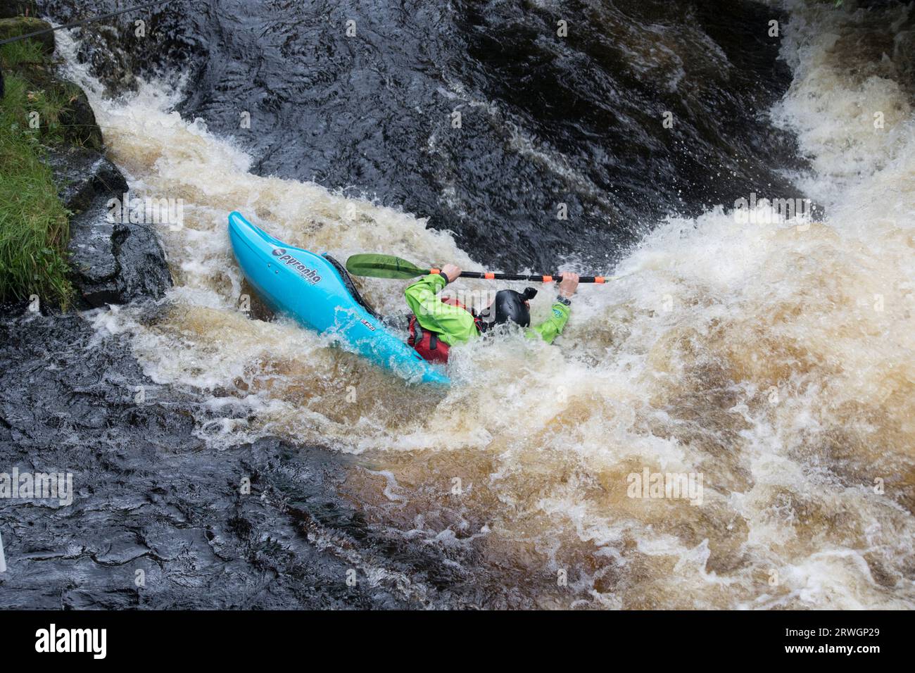 Kanufahren im blauen Slalomkanu und der grünen Jacke auf den Stromschnellen Whitewater Slalom Kanufahren im River Tryweryn im HE National Whitewater Centre in der Nähe Stockfoto