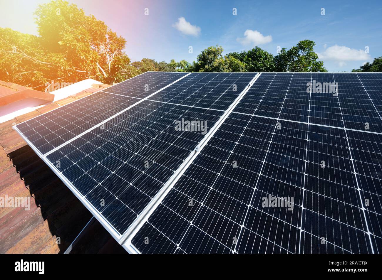 Thema "Ökostrom". Solaranlage auf dem Hausdach in blauem Himmel und grünem Baumhintergrund Stockfoto